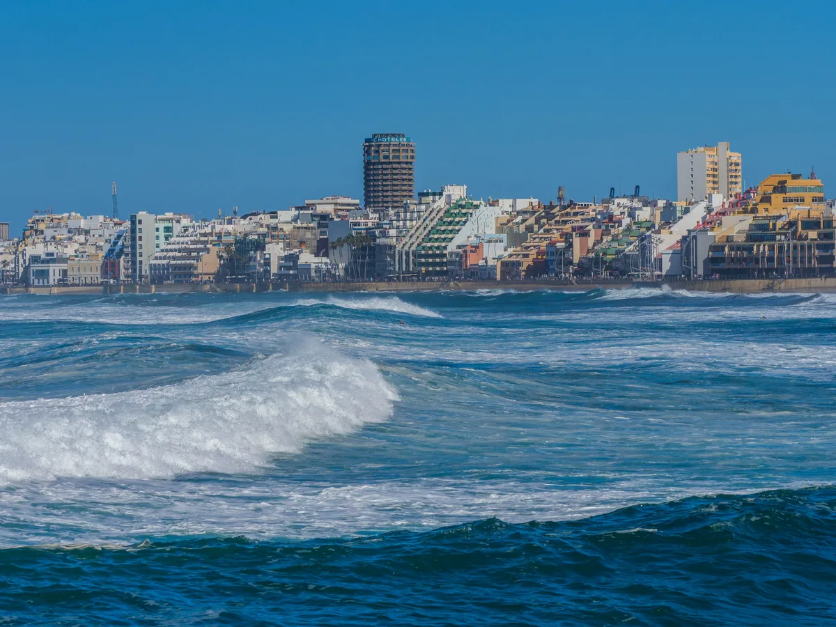 White Atlantic surf rolling in at Las Canteras with the high-rise seafront of Las Palmas on the far shore.