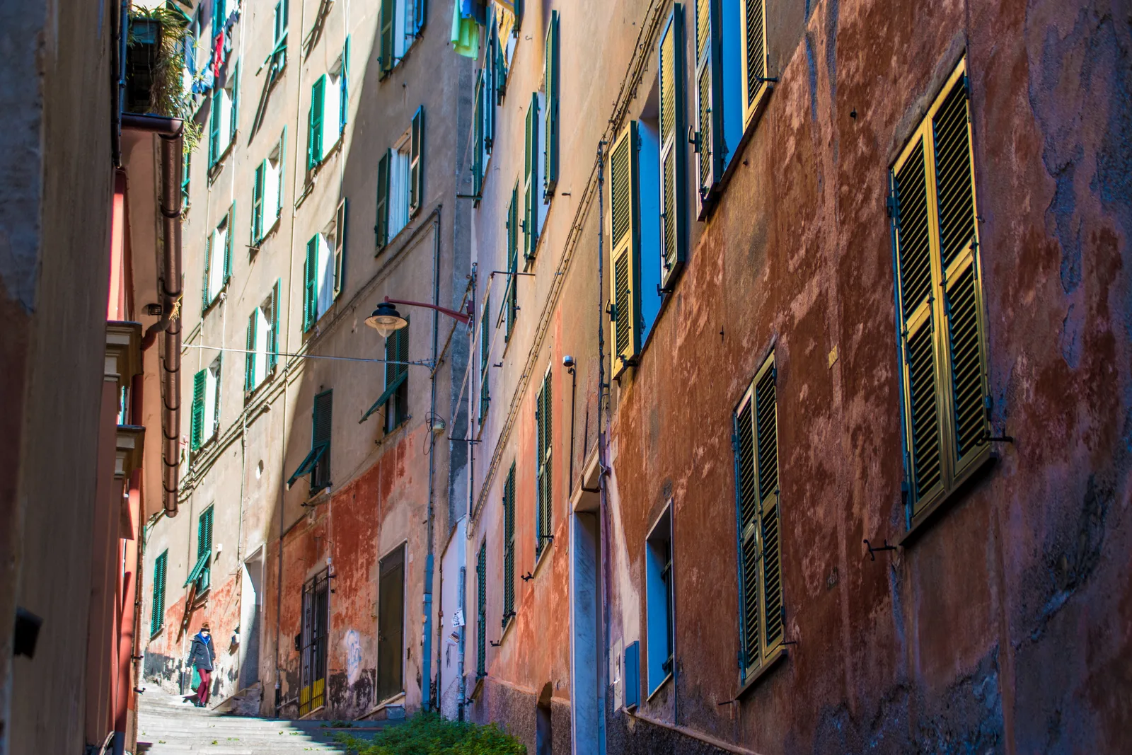 A tall weathered facade with green shutters in Genoa's old town alleys.