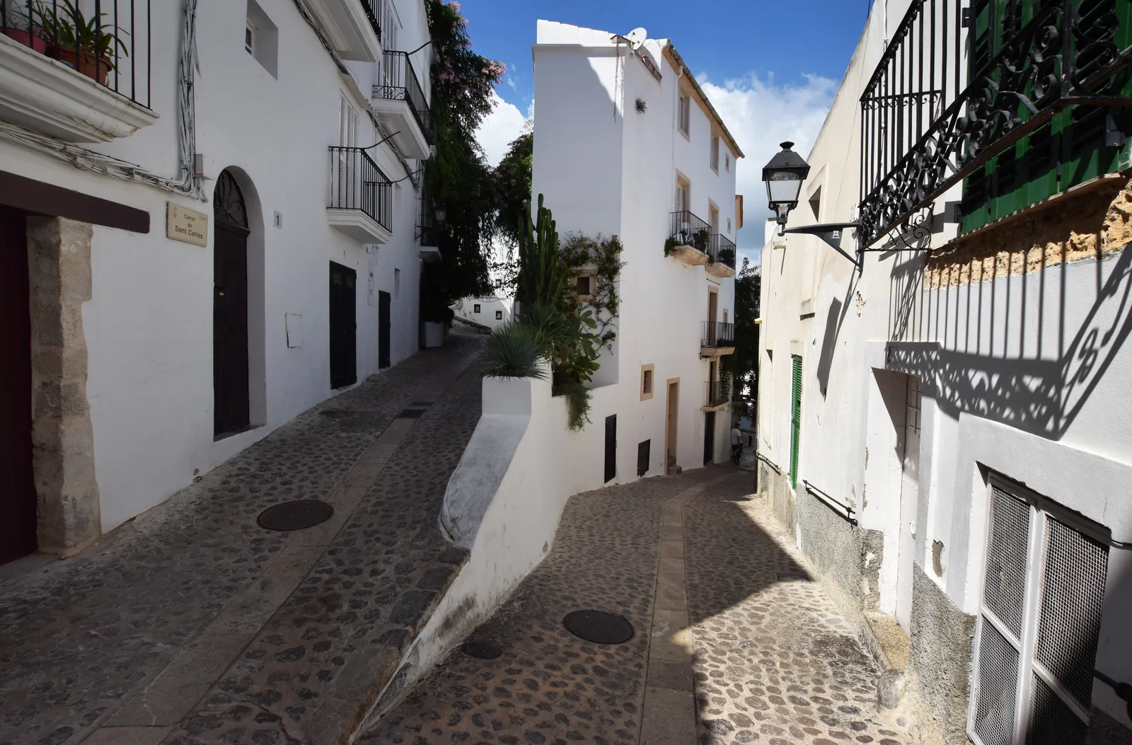 A cobbled bend in an Ibiza old-town street between white houses and balconies.