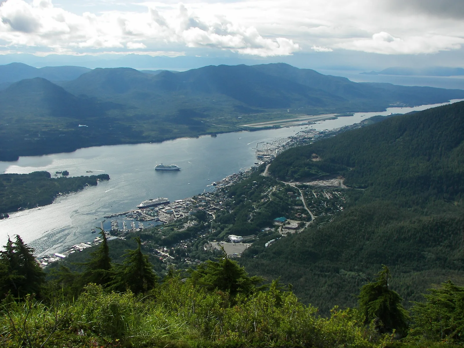 View from a hillside over Ketchikan and the Tongass Narrows, with the town along the shore and mountains beyond.