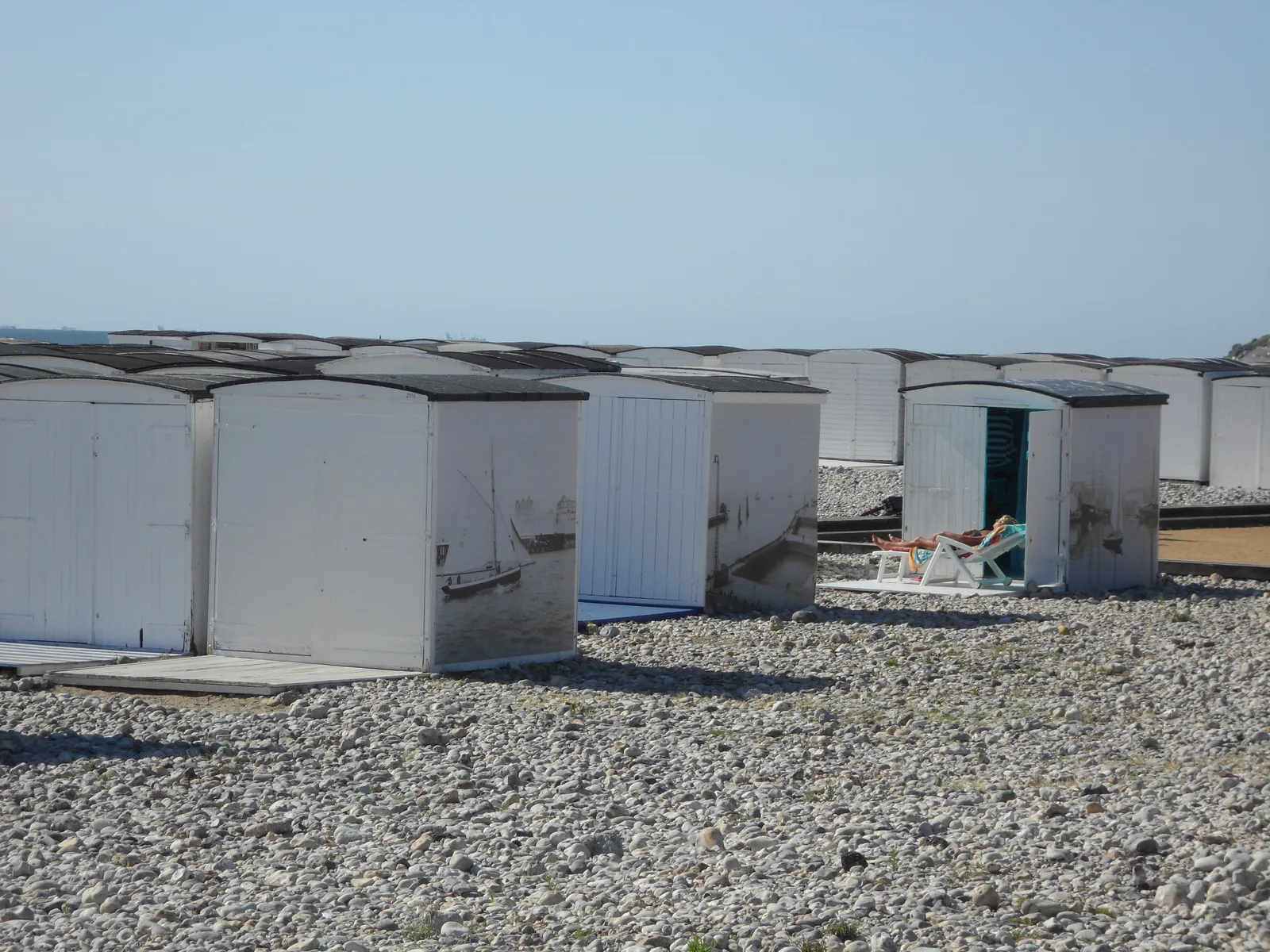Weathered white beach huts lined up on the shingle at Le Havre.