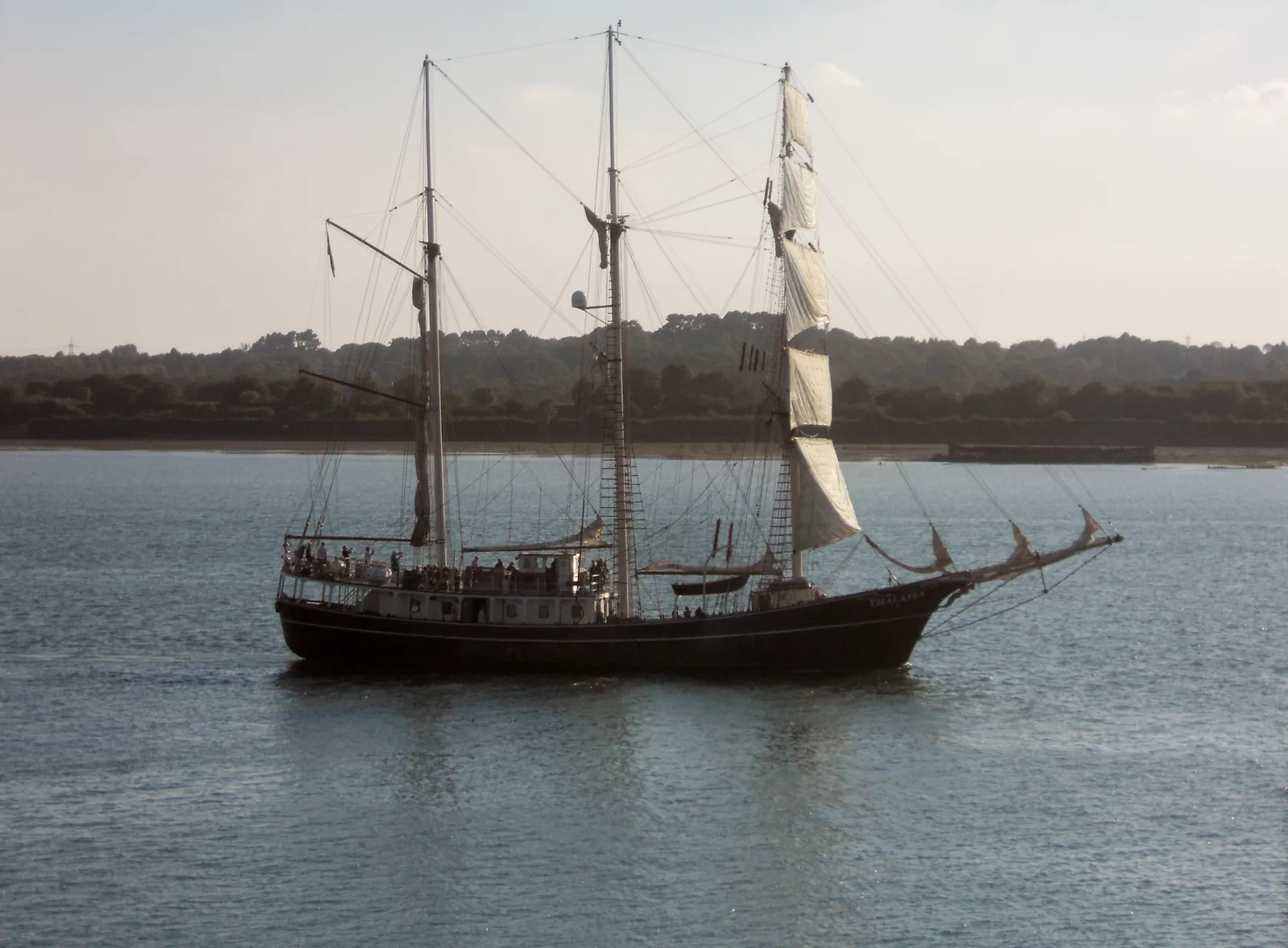 A three-masted sailing ship on Southampton Water with a wooded shore behind.