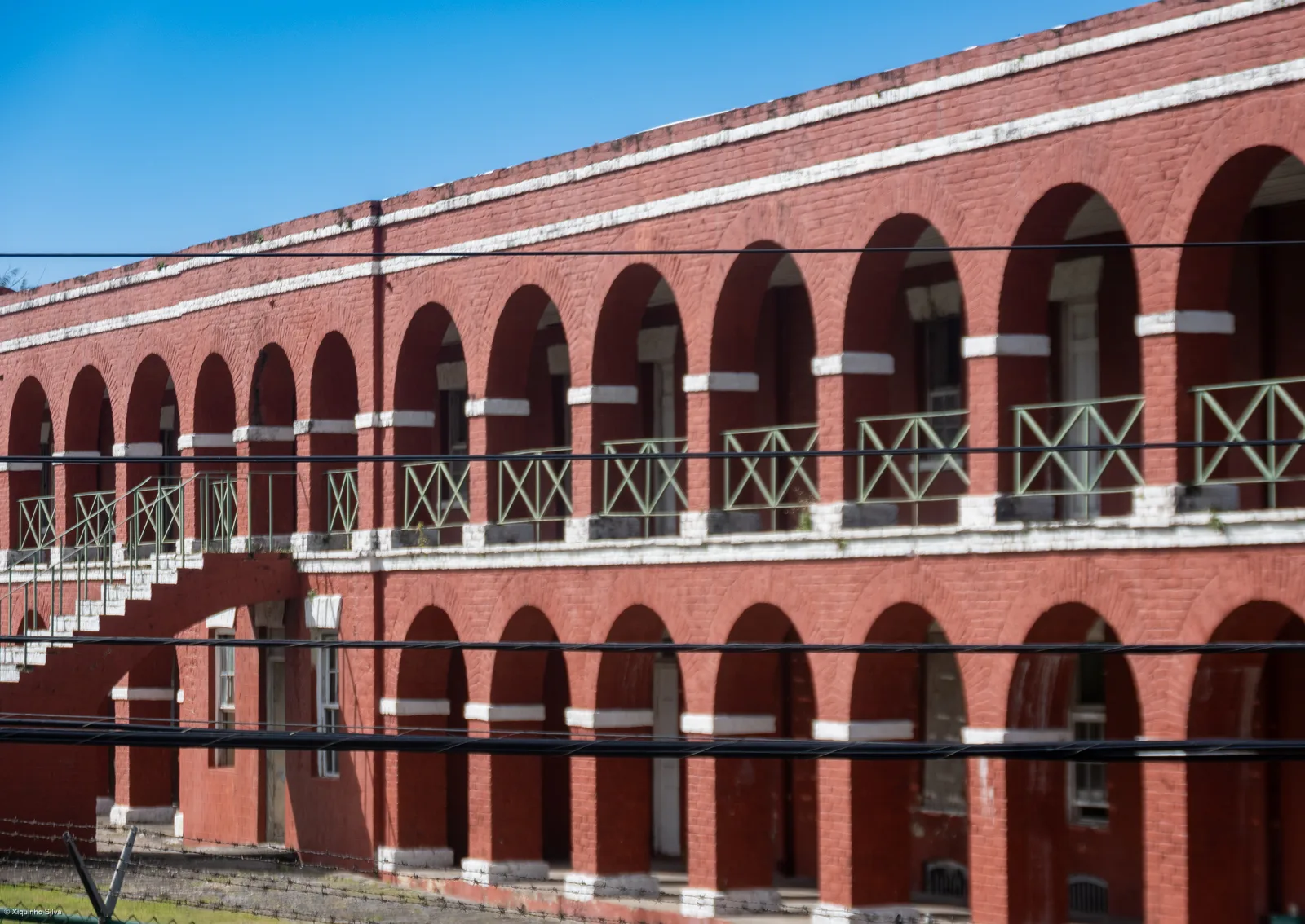 A long red brick two-storey arcade with white balustrades under a blue sky at the Garrison in Historic Bridgetown.