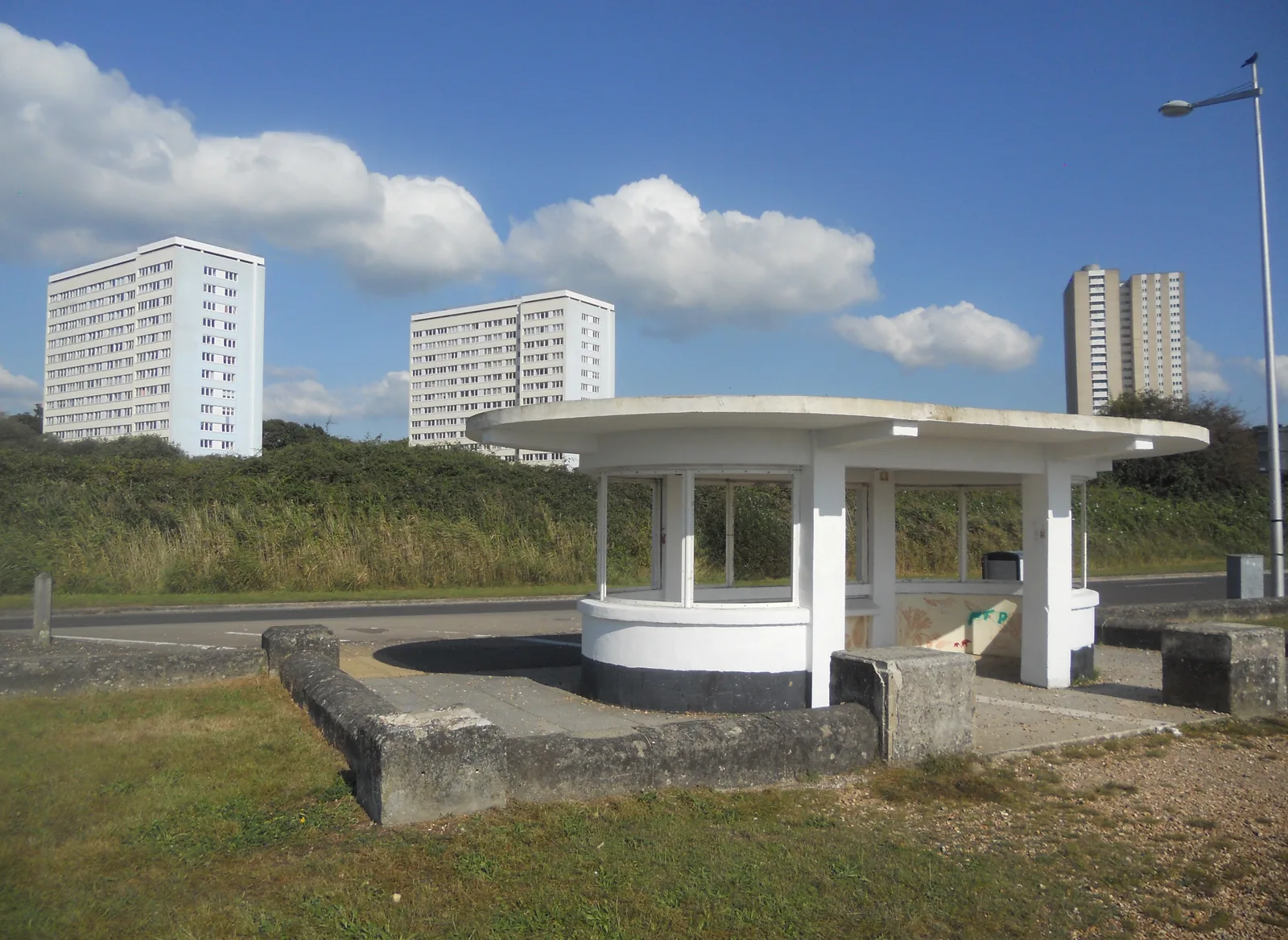 A white 1930s seafront shelter on the Weston shore at Southampton with tower blocks behind.