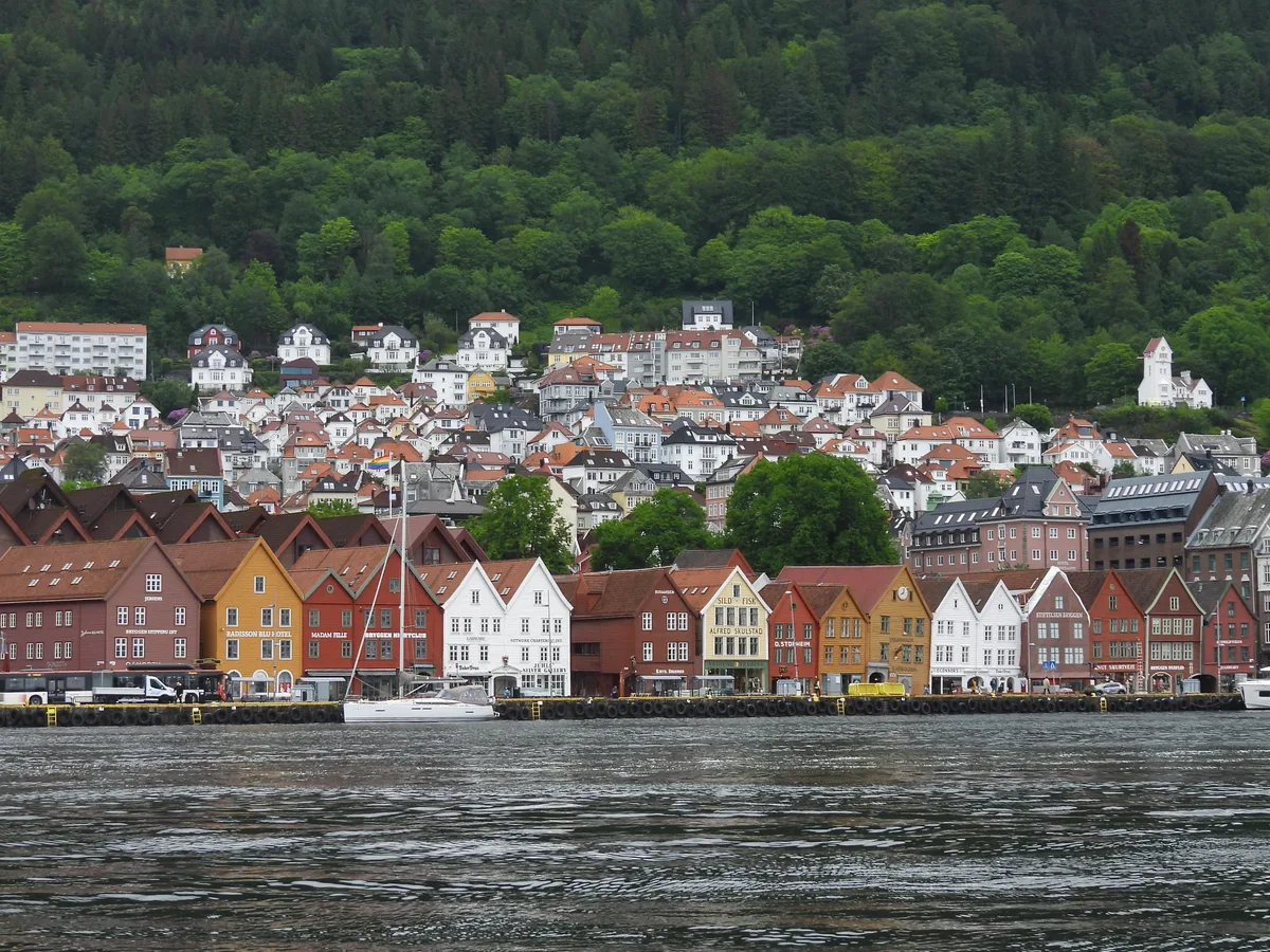 Colourful wooden Bryggen wharf buildings along Vagen harbour in Bergen with houses climbing the green hillside behind.