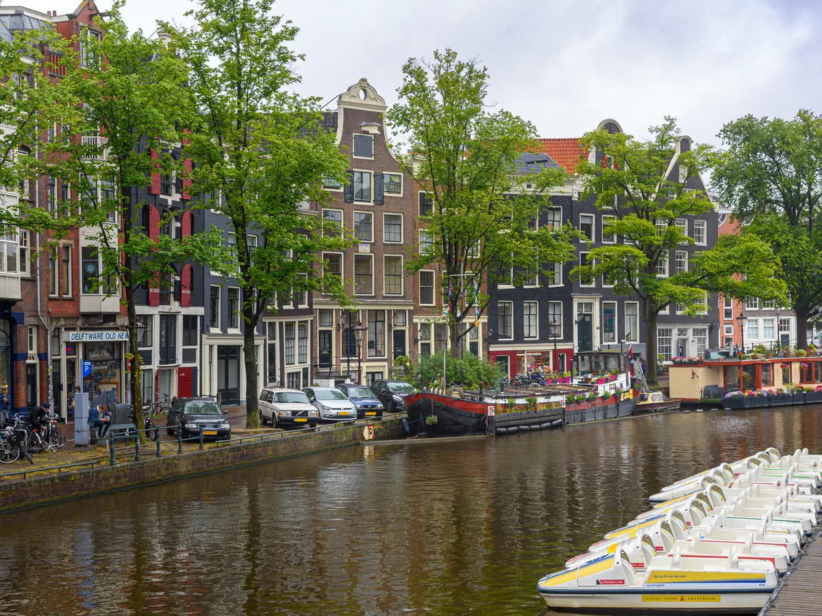 A tree-lined stretch of Prinsengracht with gabled houses and white pedal boats in the foreground.