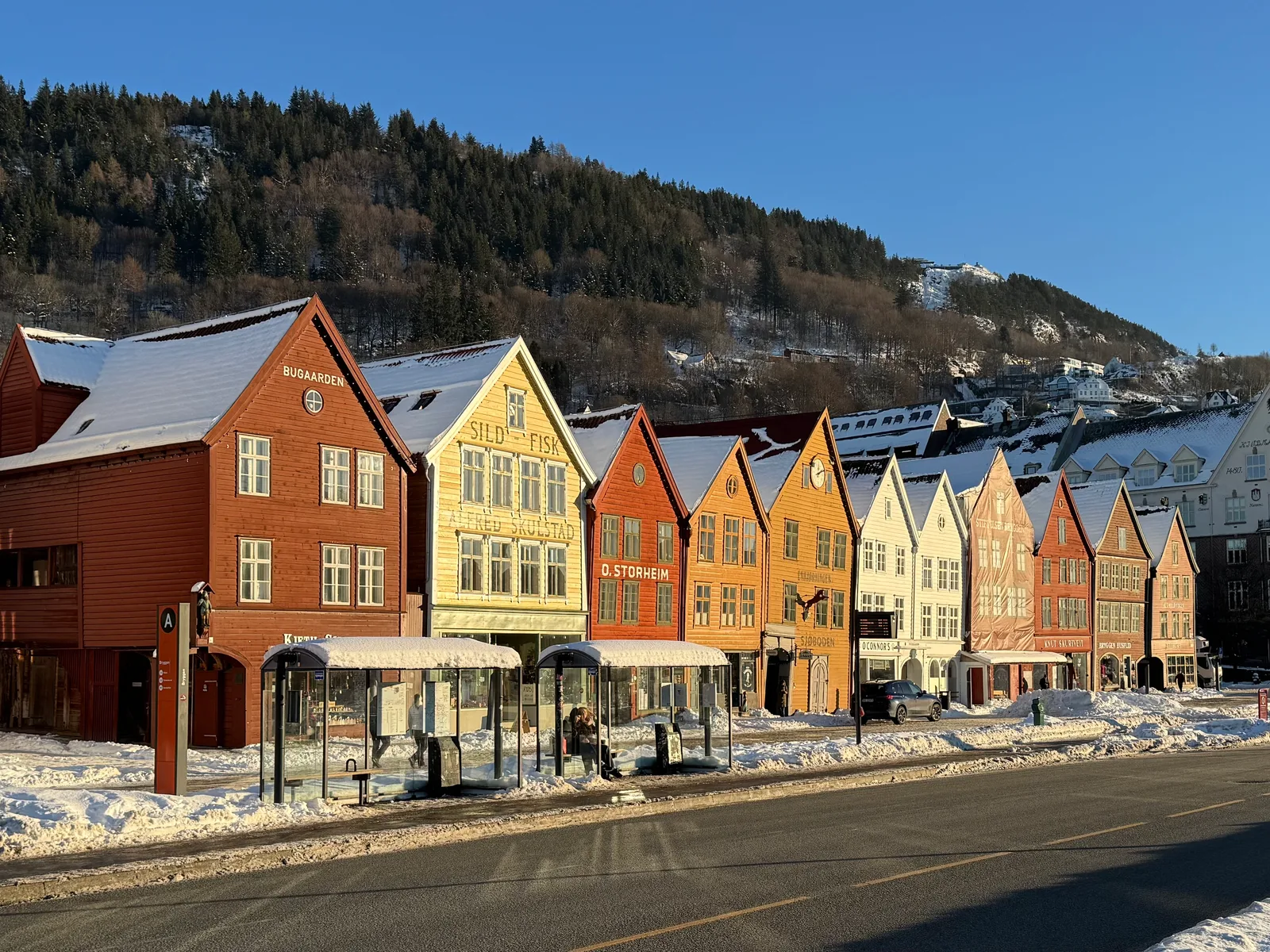 The Bryggen wharf buildings in winter light on Bergen's waterfront with snow on the roofs and an empty plaza.