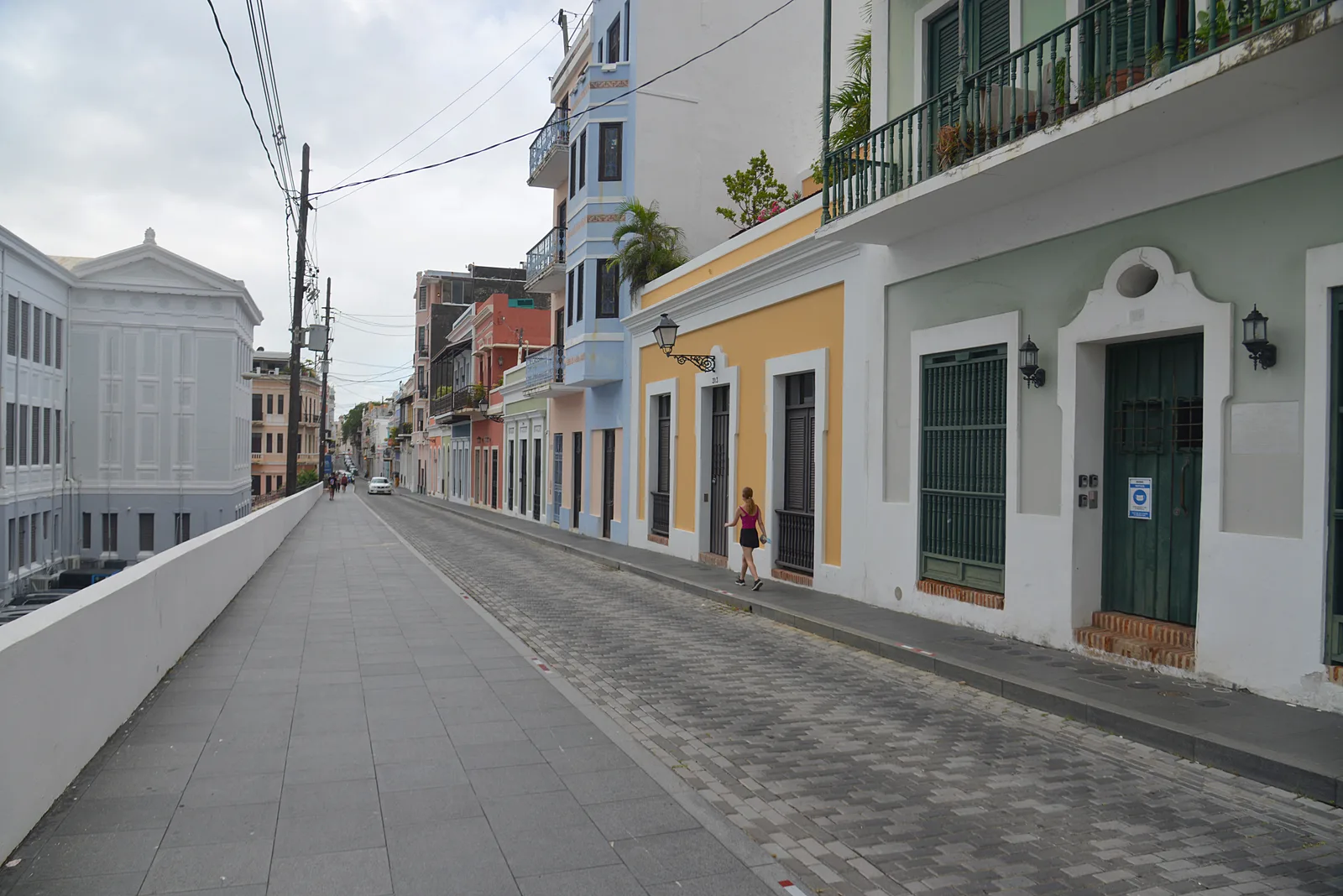 A long cobbled and paved lane lined with pastel colonial houses runs along an old wall in Old San Juan.