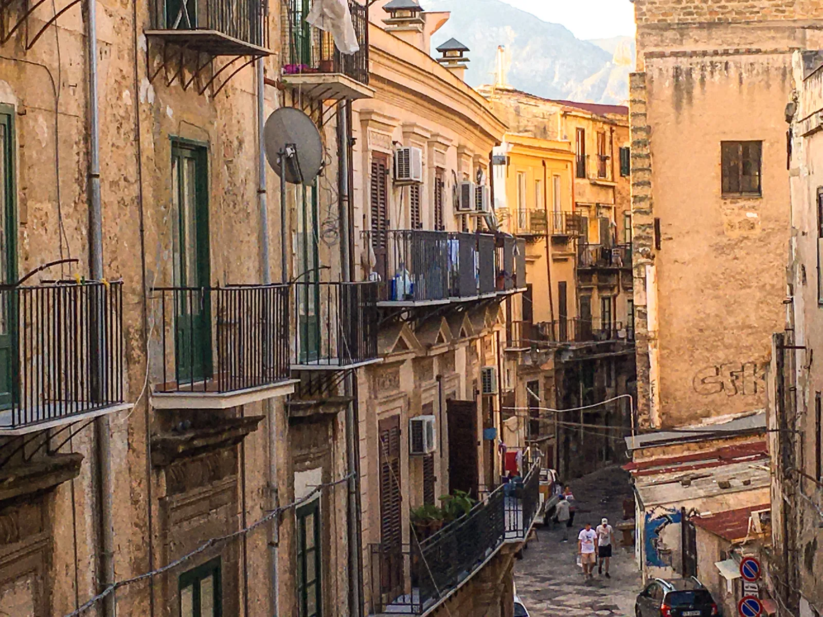 A narrow Palermo old-town street seen from above, lined with balconied ochre buildings.