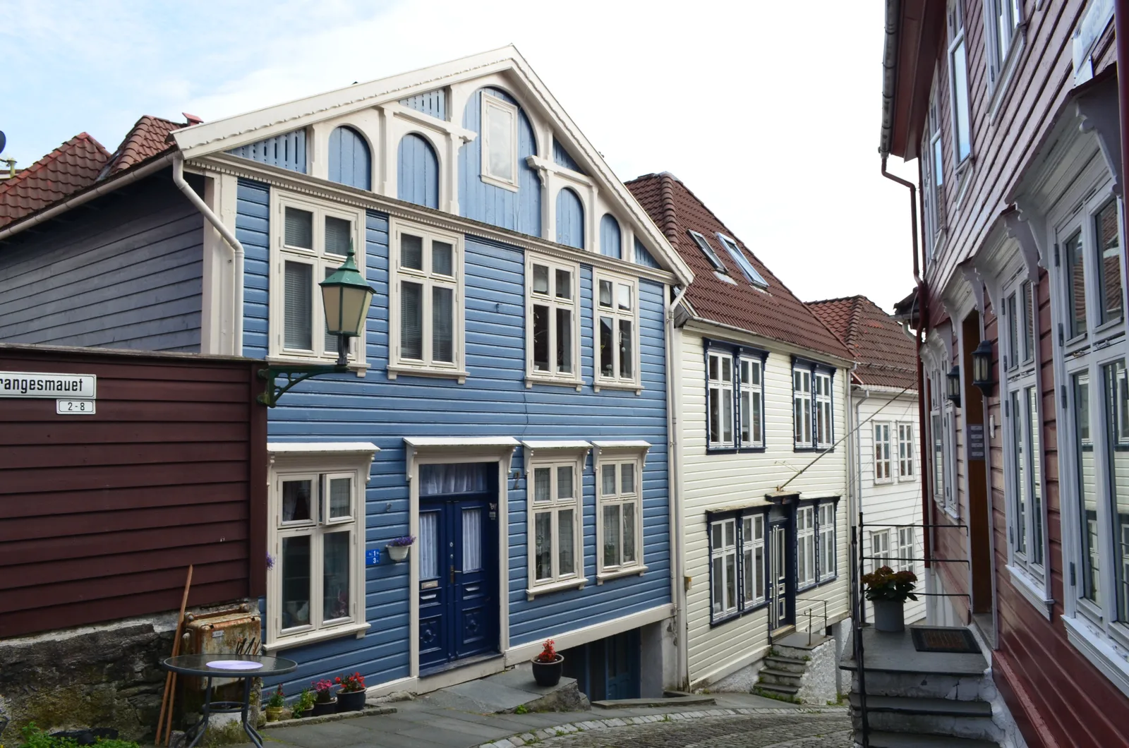 A blue timber house on a Bergen lane with a vintage street lamp and a street sign on the left.