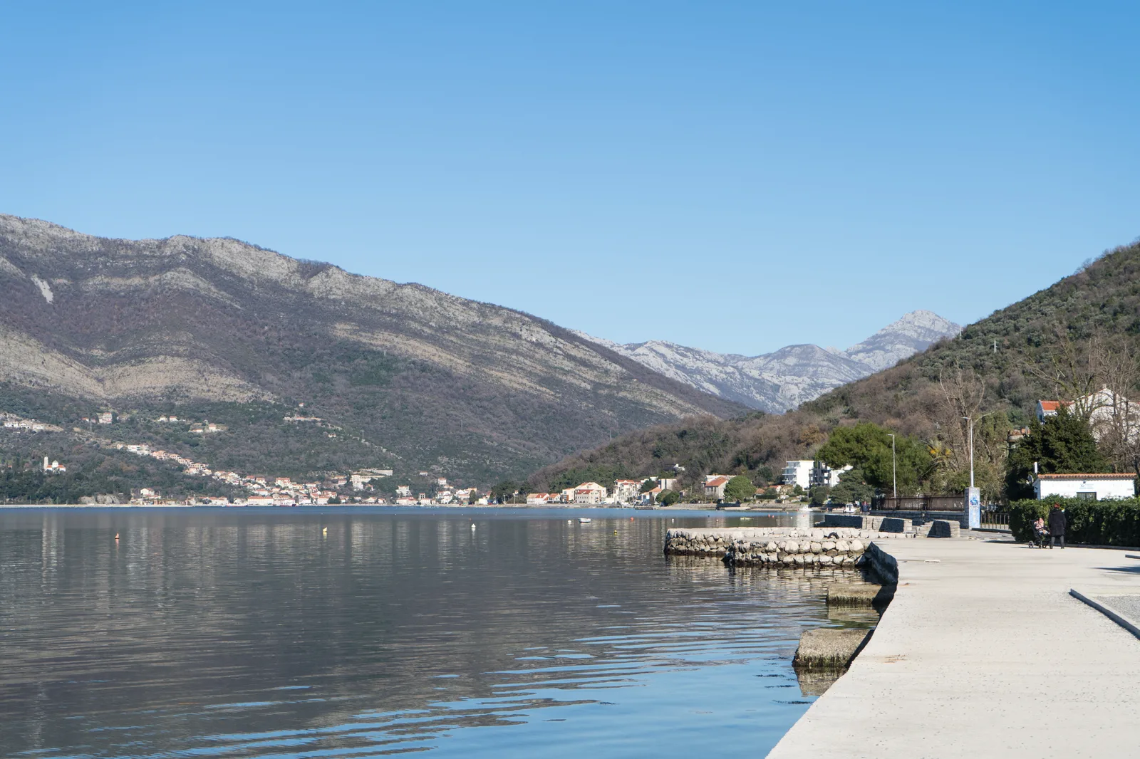 An empty seaside promenade at Donja Lastva looking along the Bay of Kotor toward mountains.