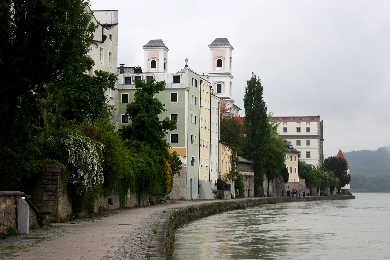A tree-lined path along the Inn promenade in Passau with colourful old-town buildings beside the river.