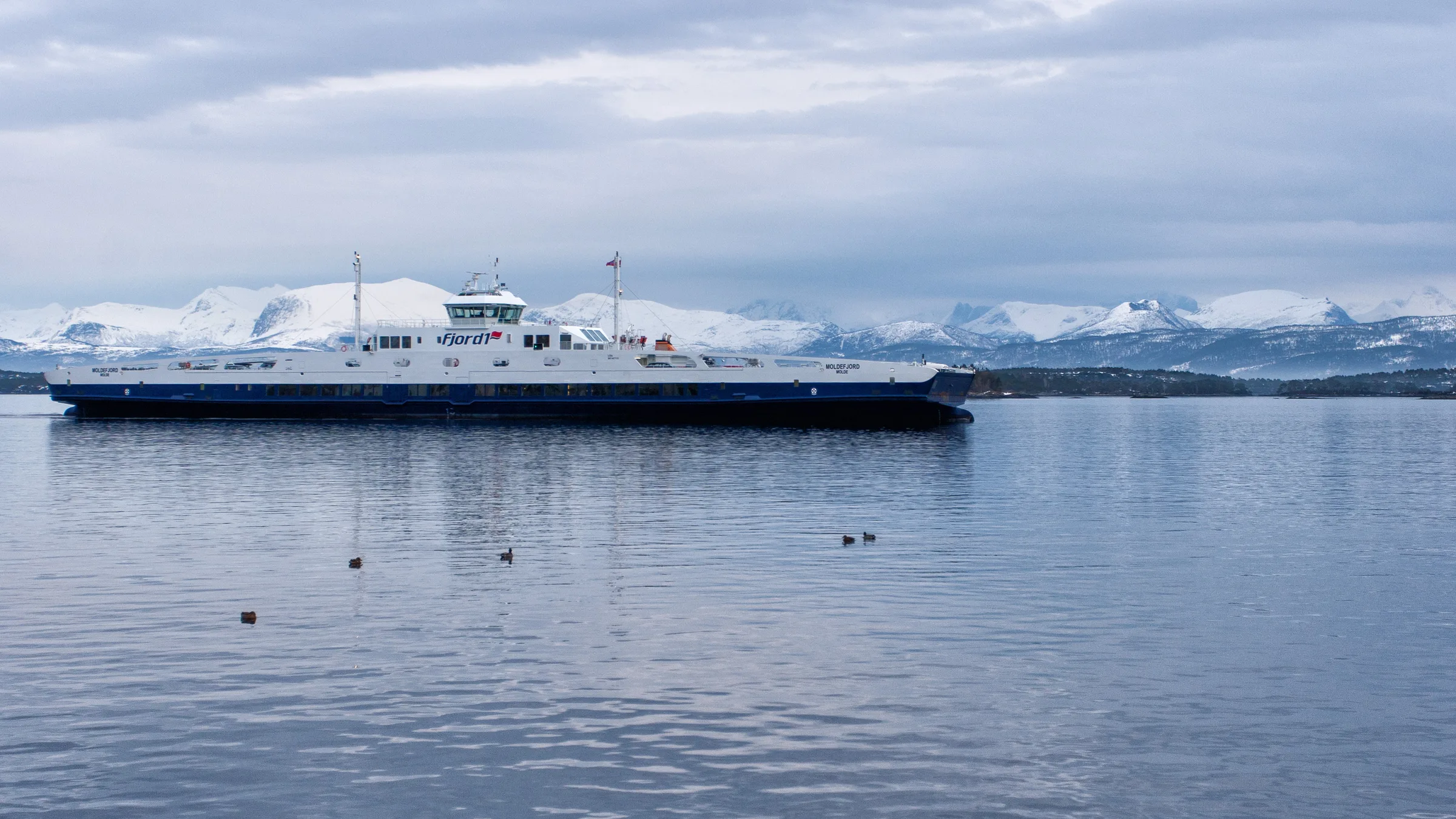 A ferry crossing the calm Molde fjord with the snow-capped Romsdal Alps behind.