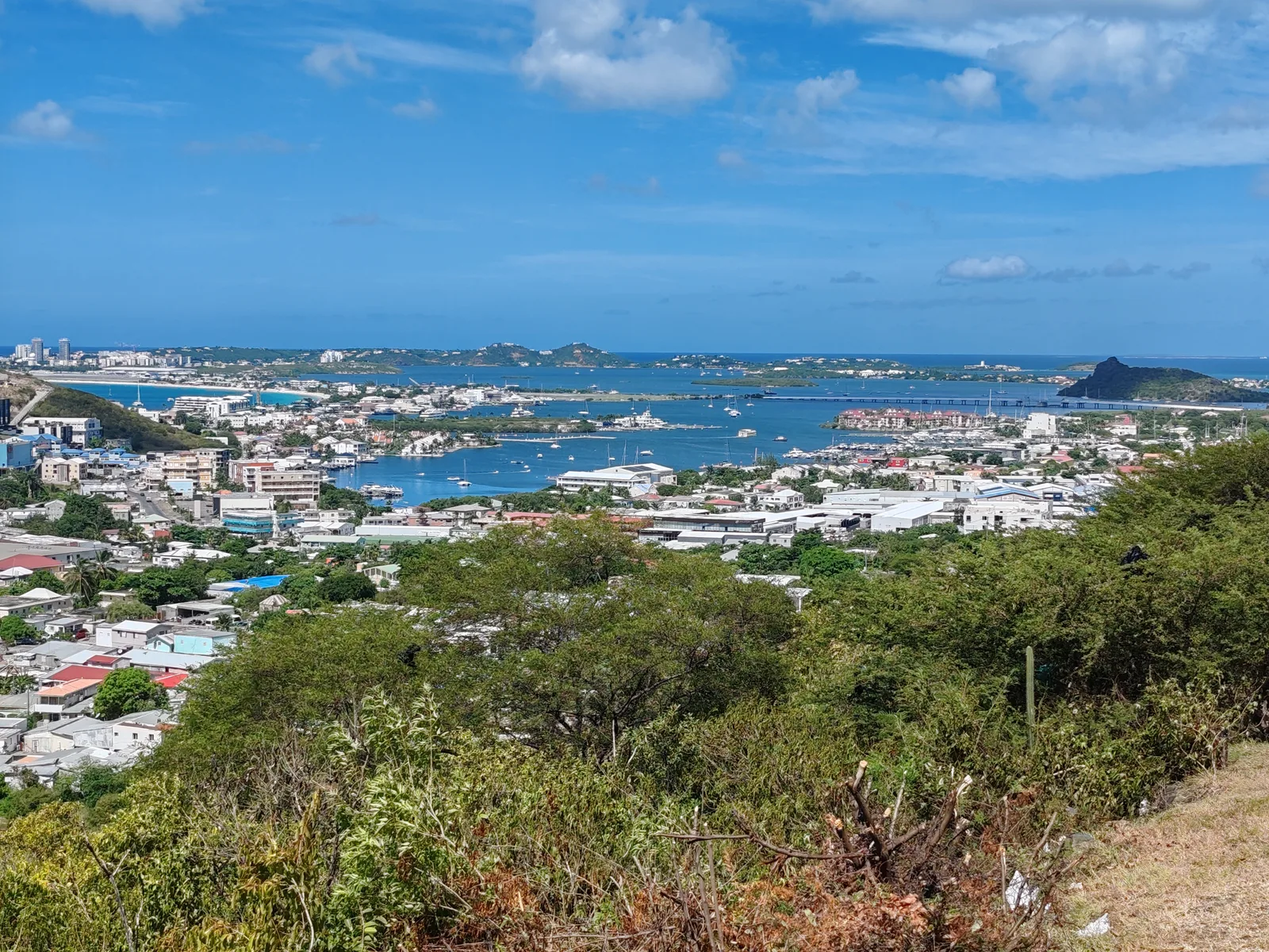 A calm lagoon surrounded by green hills on Sint Maarten under a cloudy sky.