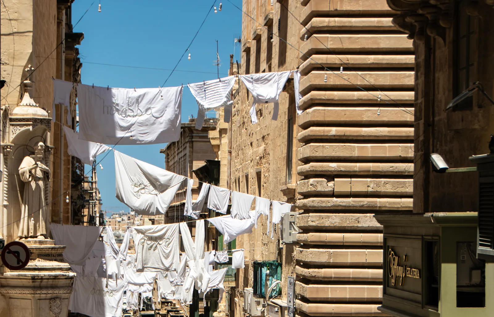 Washing strung across a Valletta street under a sunny sky.