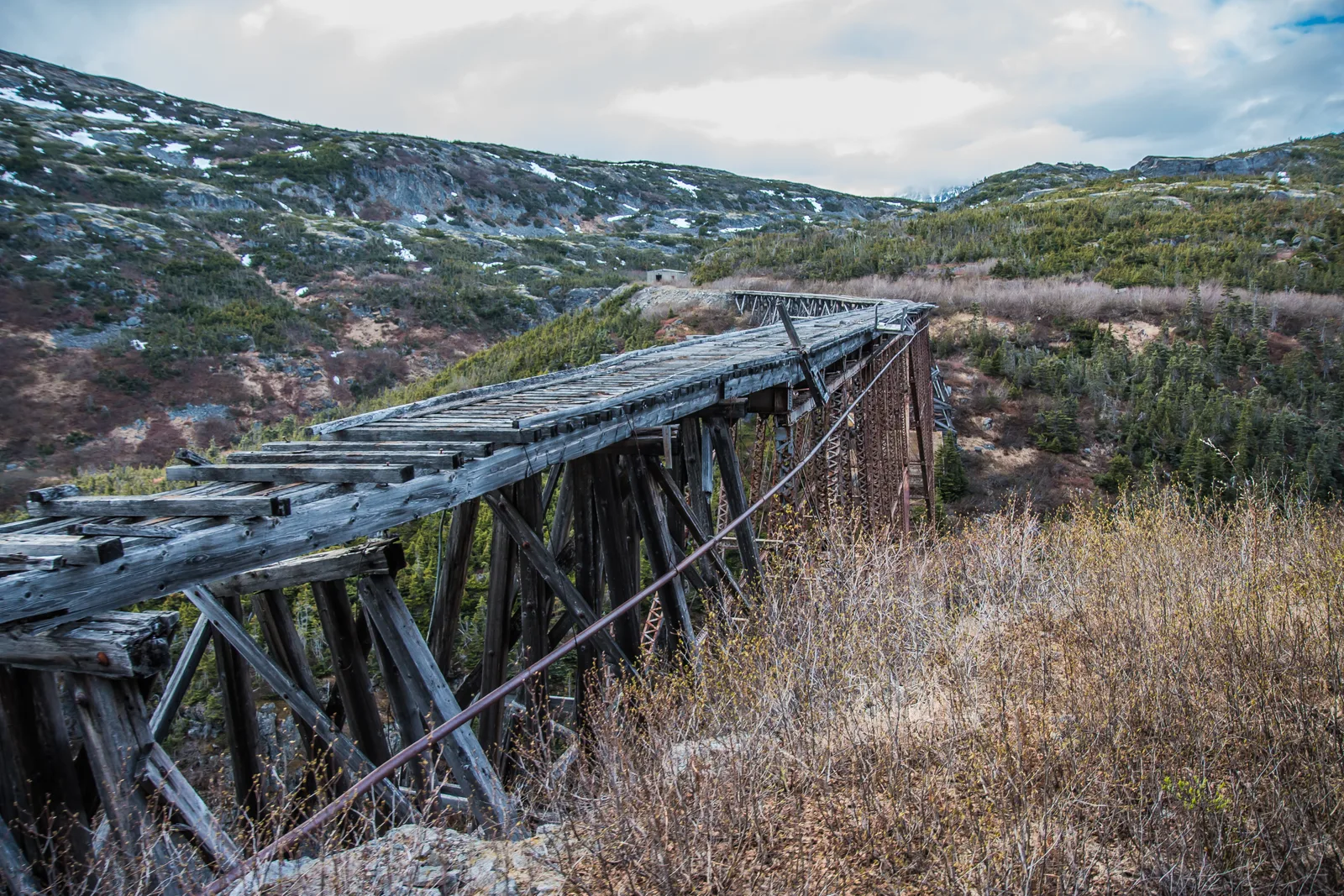 A weathered wooden railway trestle running across a barren, rocky mountain slope near White Pass.