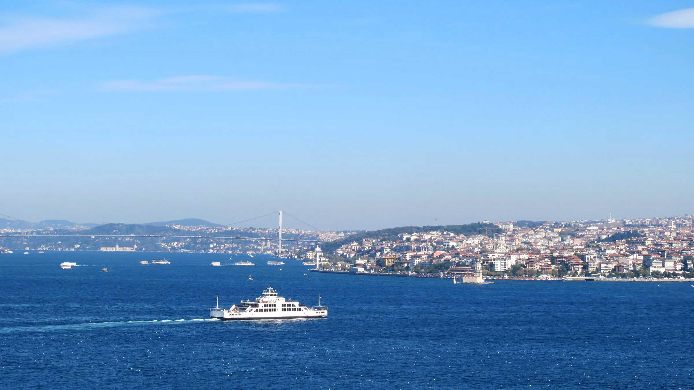A white ferry crossing the Bosphorus with Istanbul's European shore and the Bosphorus Bridge in the haze.