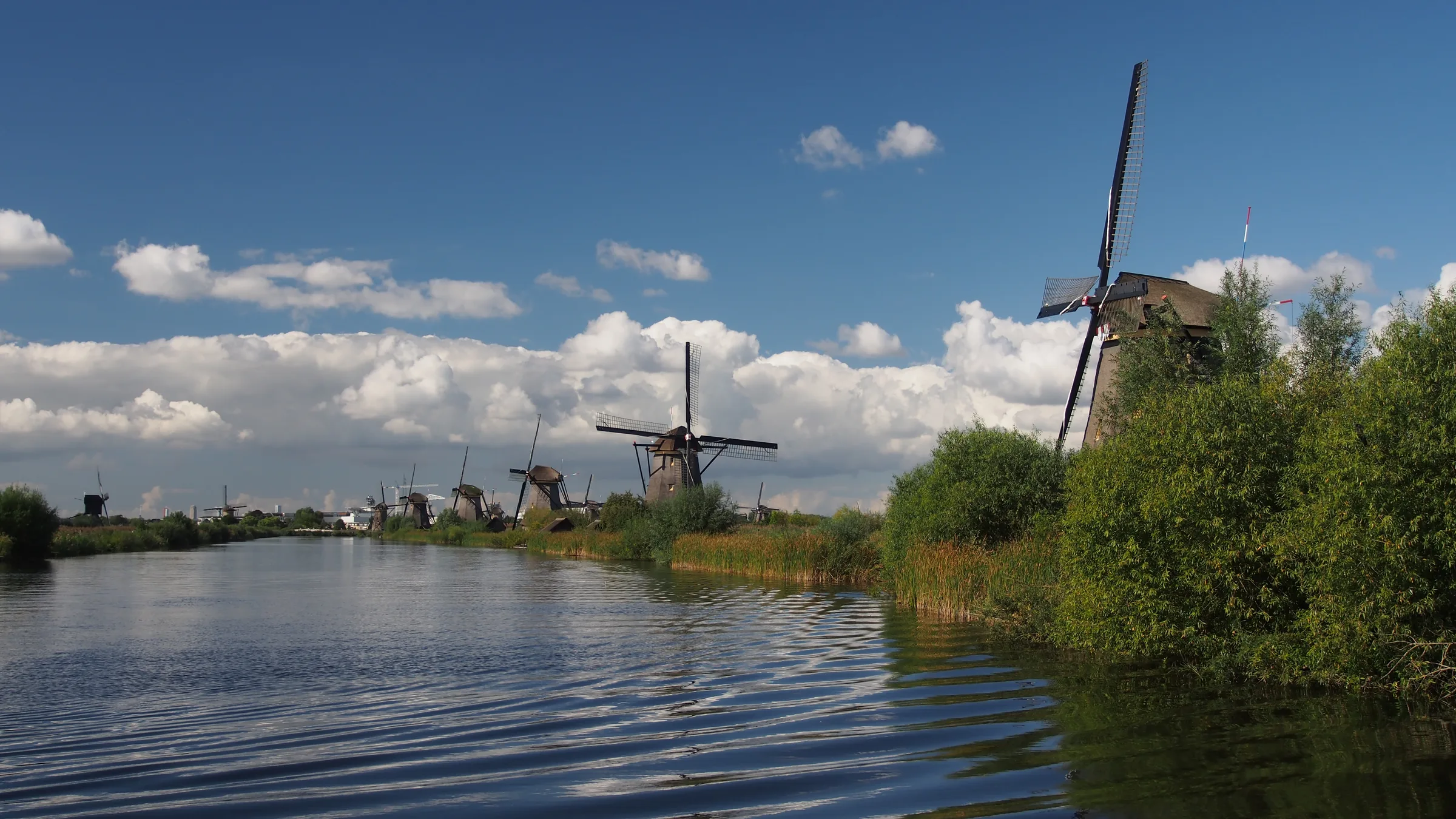 A row of historic windmills along a canal at Kinderdijk under a deep blue sky with white clouds.