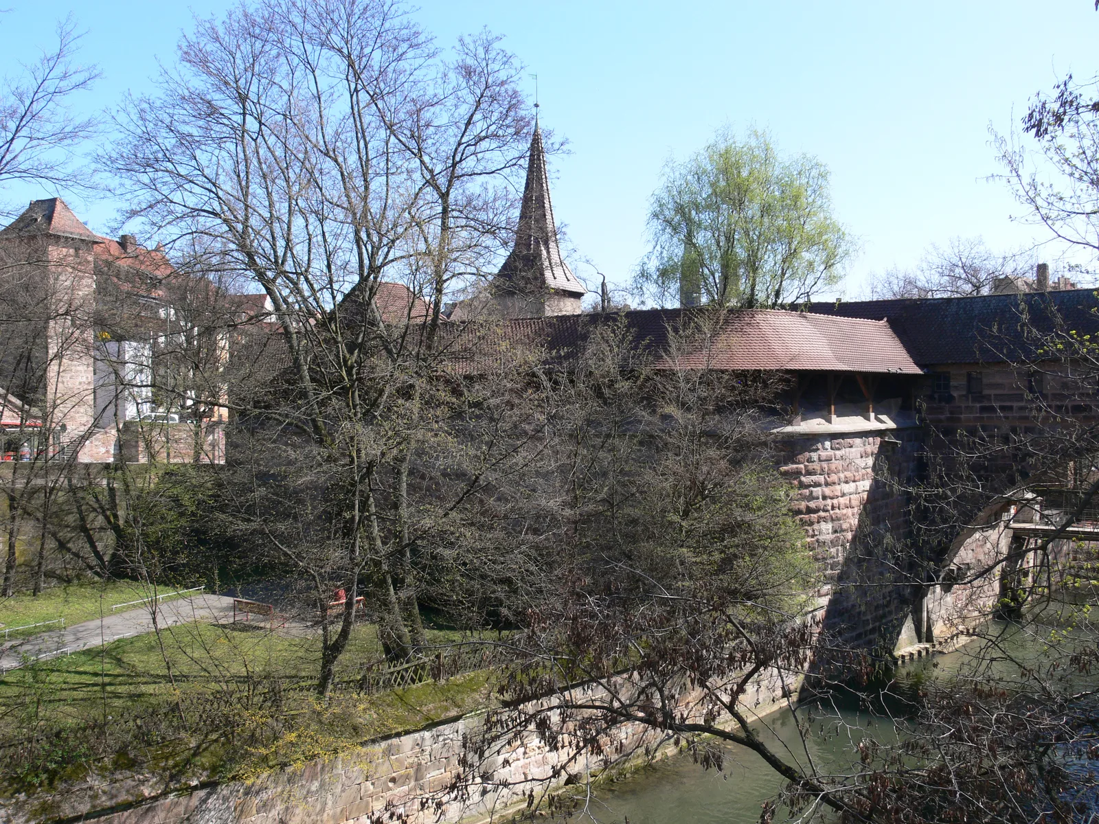 The Pegnitz river outflow beside the Hallertor with its rounded bastion in Nuremberg under trees.