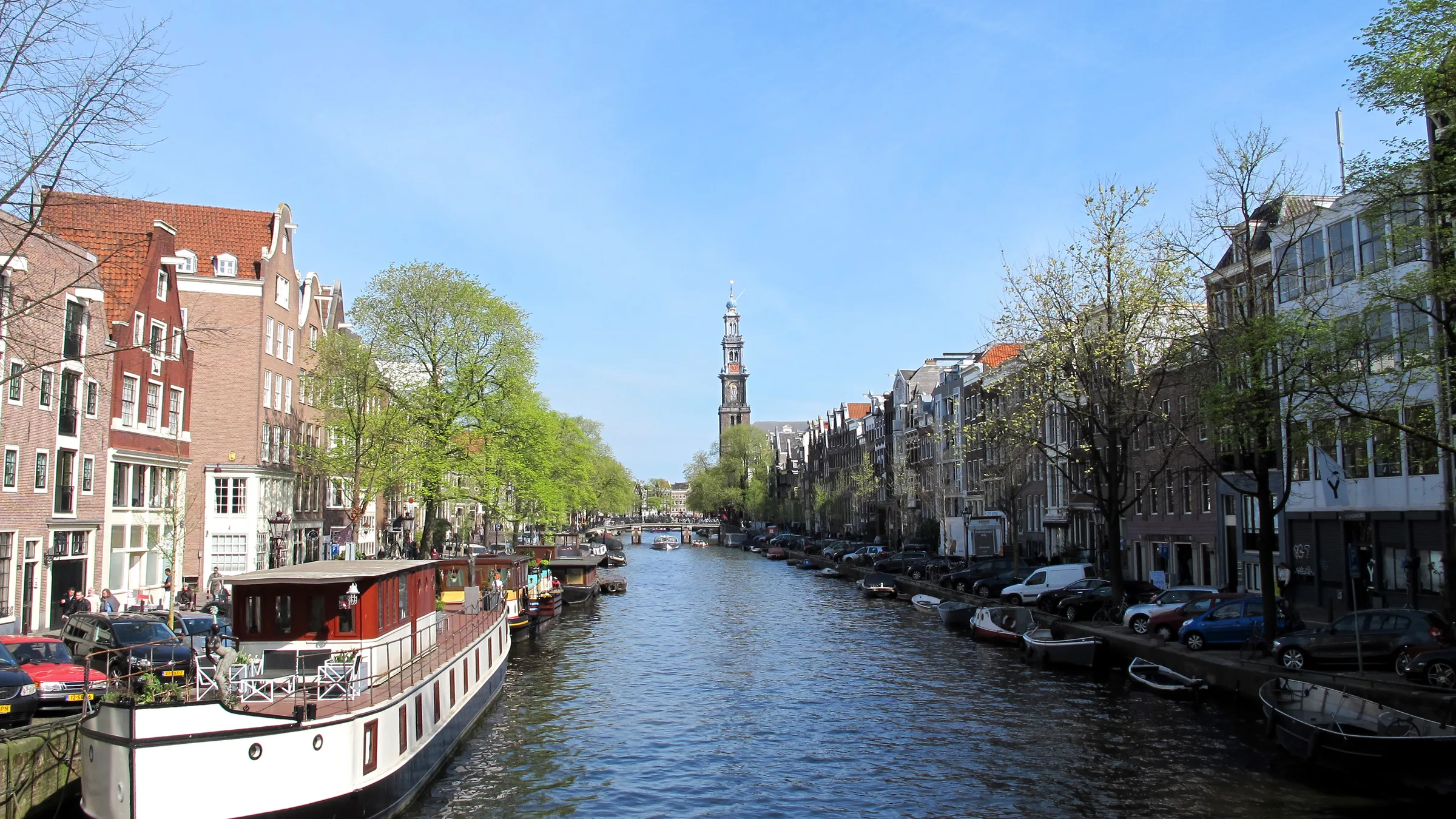 Prinsengracht in Amsterdam looking north from Berensluis with a white houseboat and the Westerkerk tower in the distance.