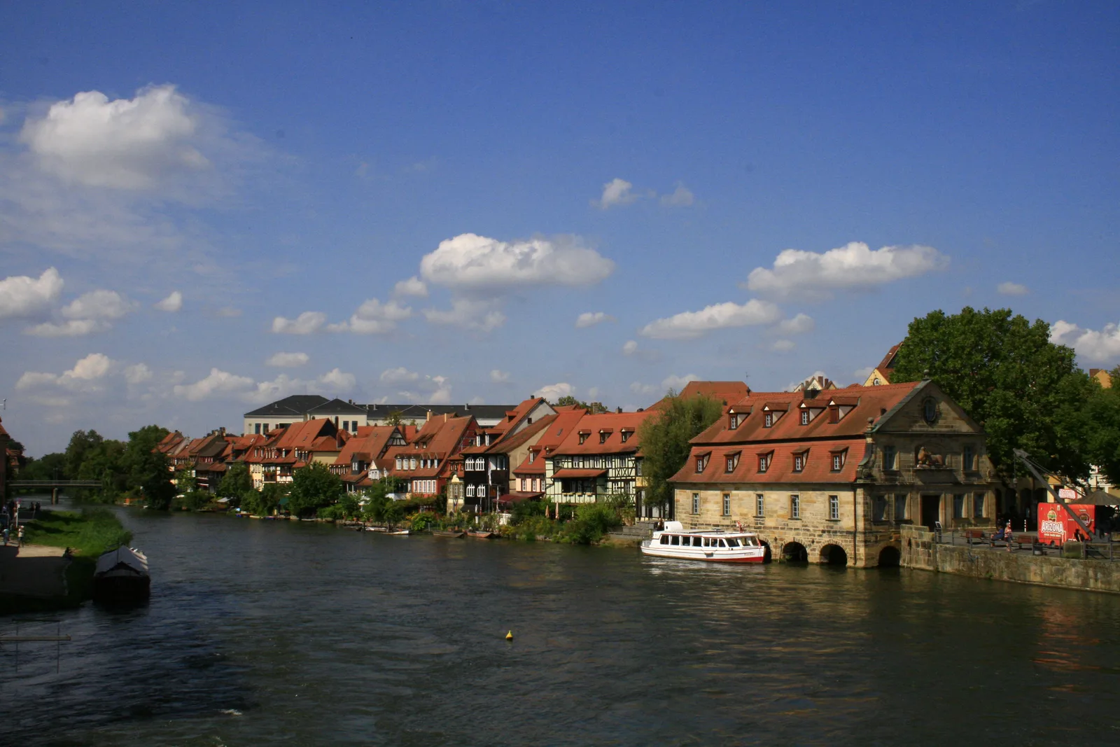 The Regnitz river in Bamberg's Little Venice with red-roofed half-timbered houses along the water and a boat moored.