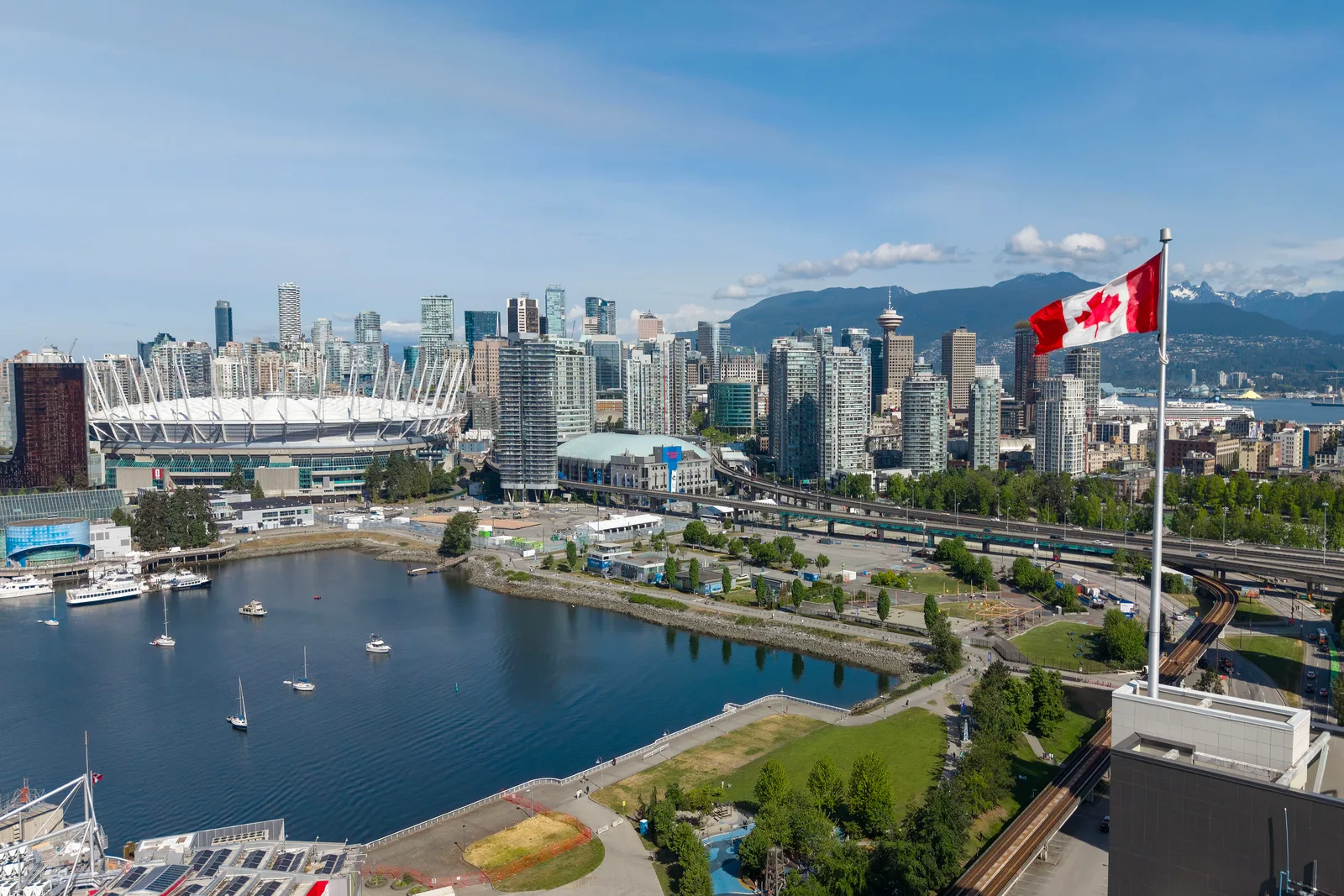Elevated view of downtown Vancouver across False Creek, with a stadium, towers, the North Shore mountains and a Canadian flag.