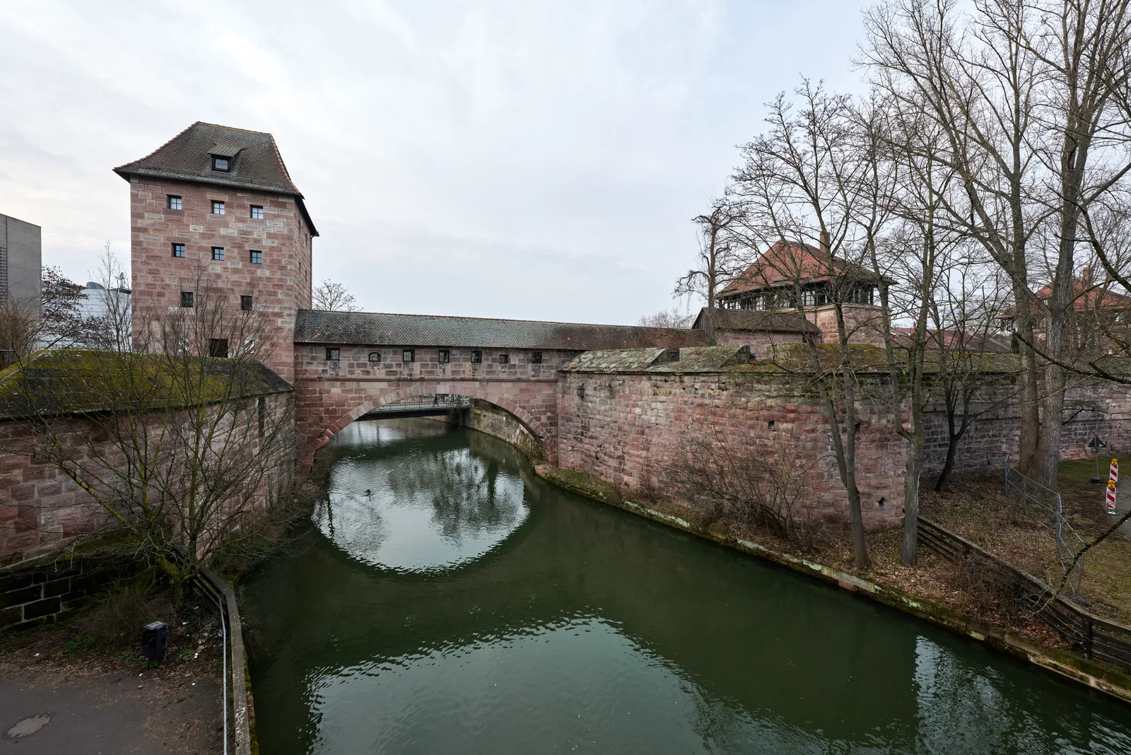 The Marientormauer city wall and a stone tower with an arch over the Pegnitz river in Nuremberg.