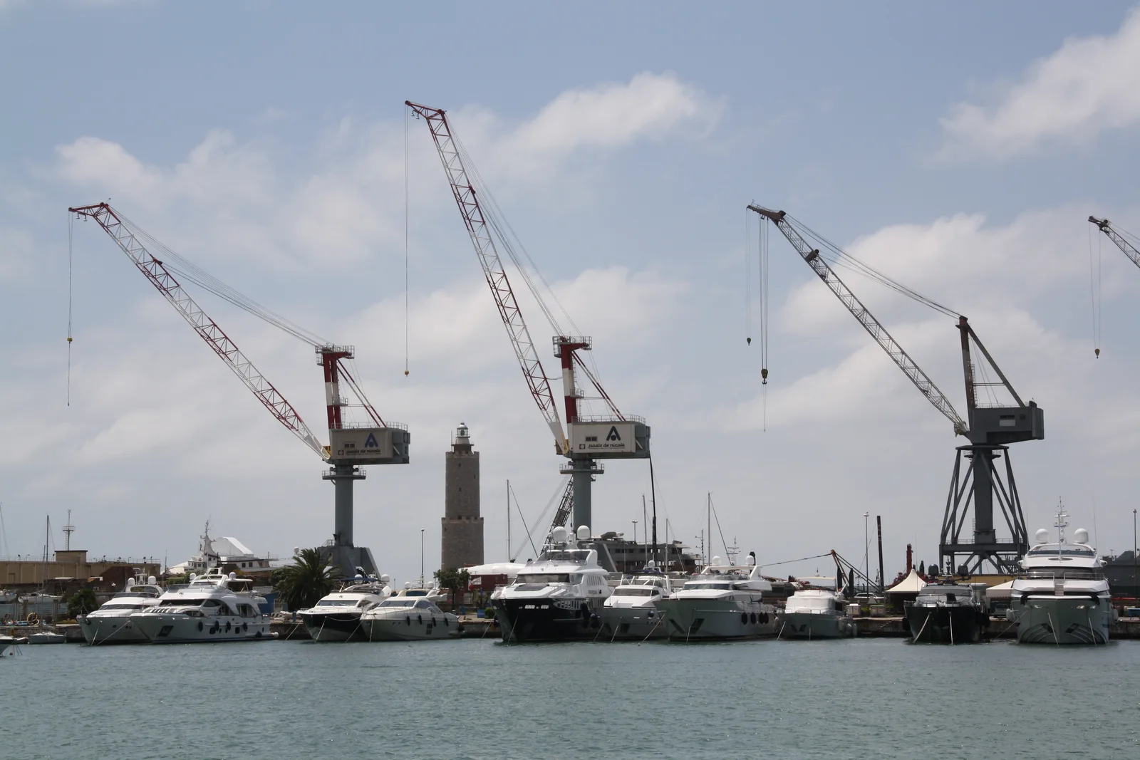 Dock cranes and yachts at the Livorno harbour with a small lighthouse in the middle distance.
