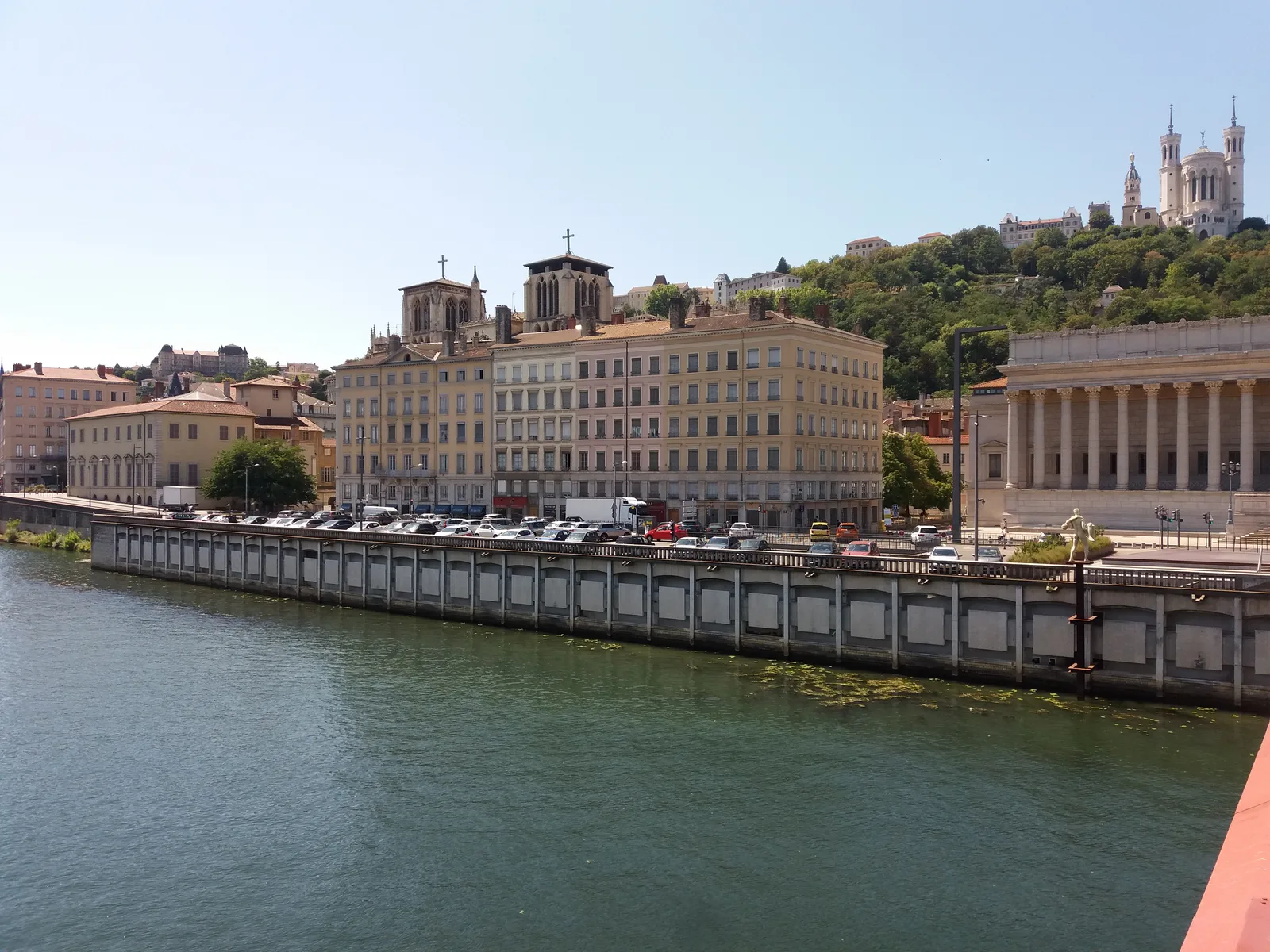 The Saône quay at Lyon with a long classical building, a colonnaded building and a church on the hill behind.