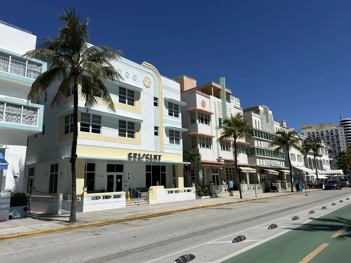 A row of pastel Art Deco hotels along Ocean Drive in South Beach with palm trees on a sunny day.