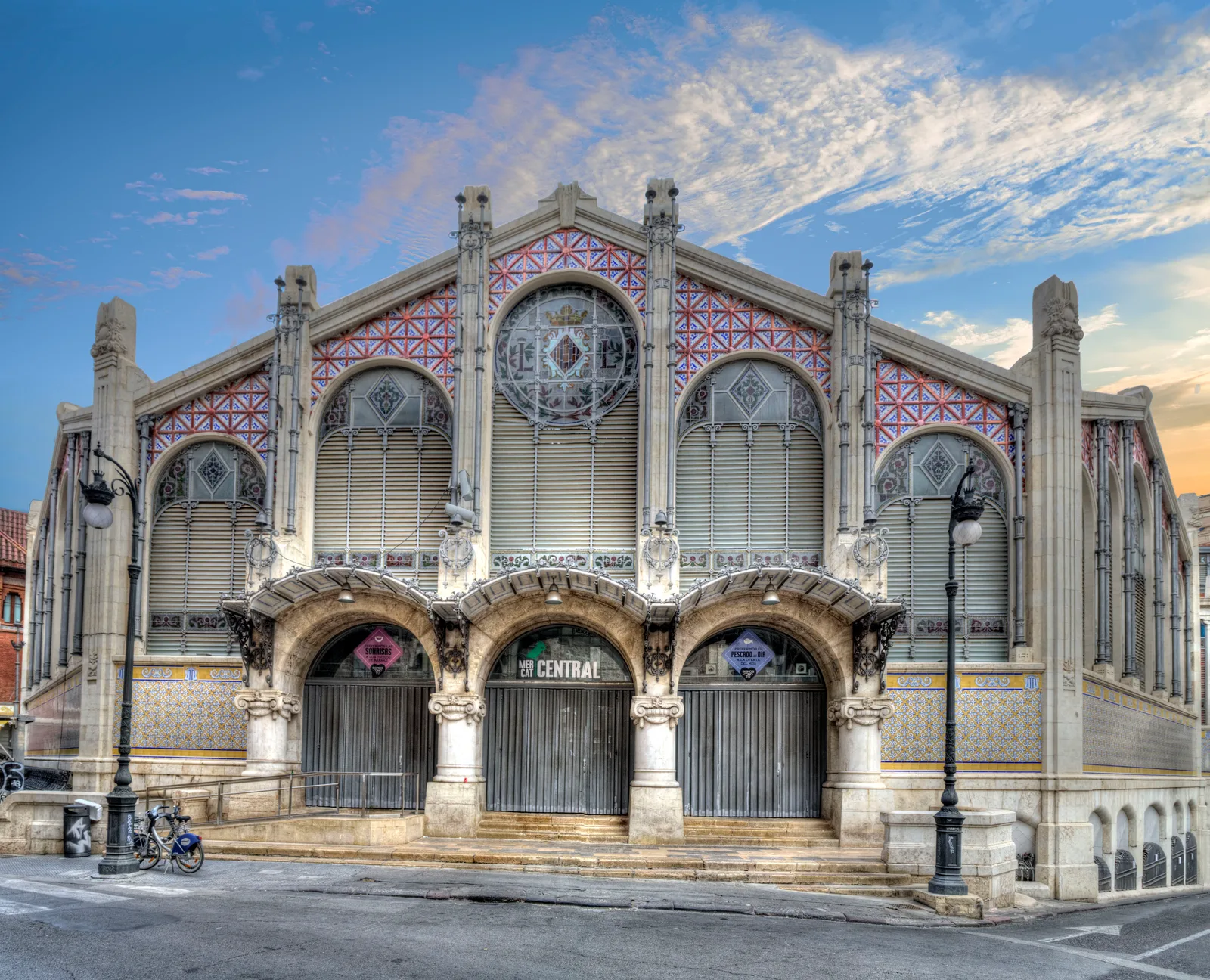 The ironwork and tilework facade of the Valencia Central Market under blue sky.
