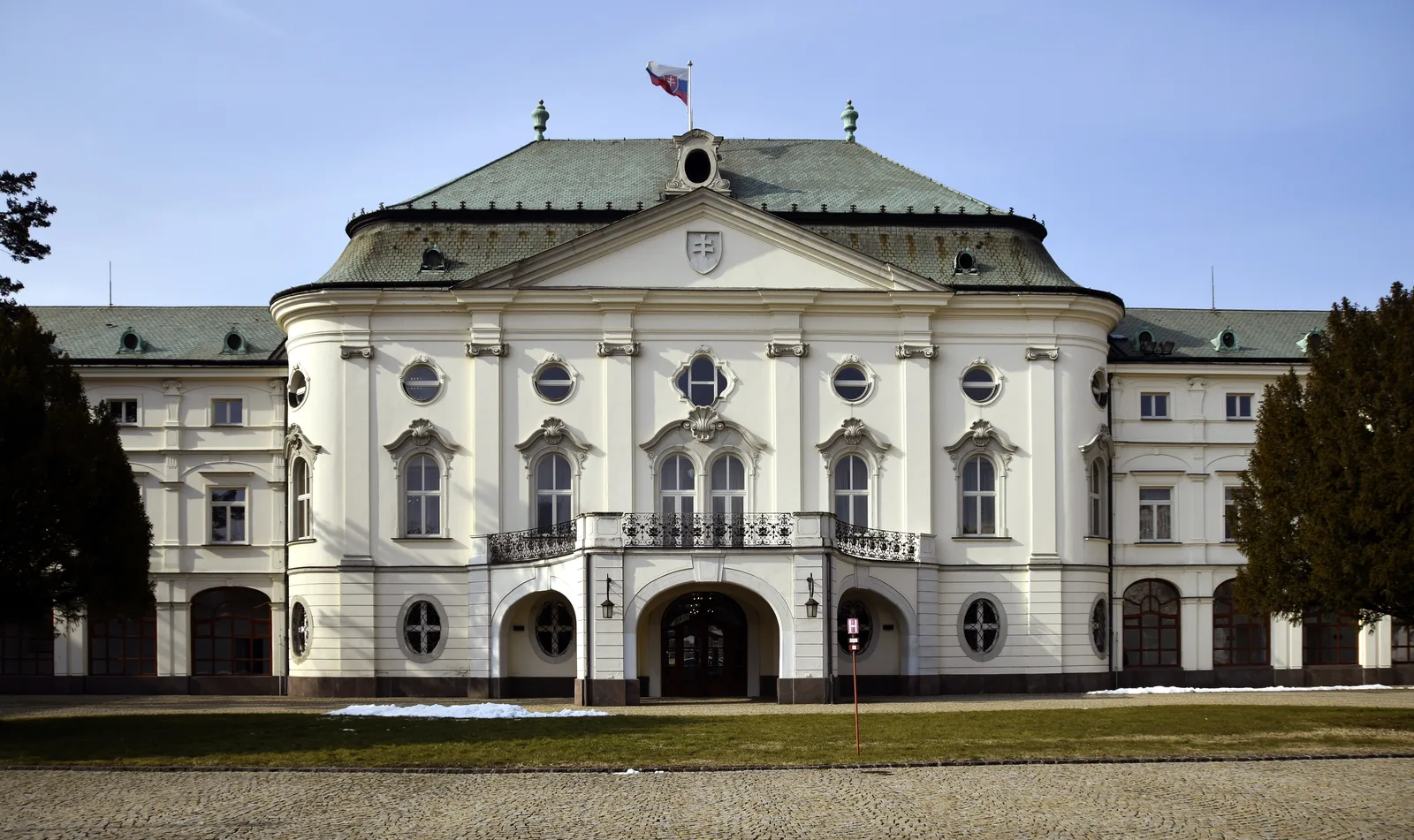 The Episcopal Summer Palace in Bratislava, a cream and white building with a green copper roof, seen from the front lawn.