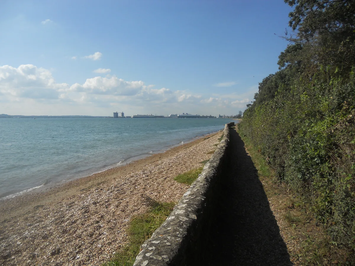 A pebble shore and low coast along Southampton Water with the port in the distance.