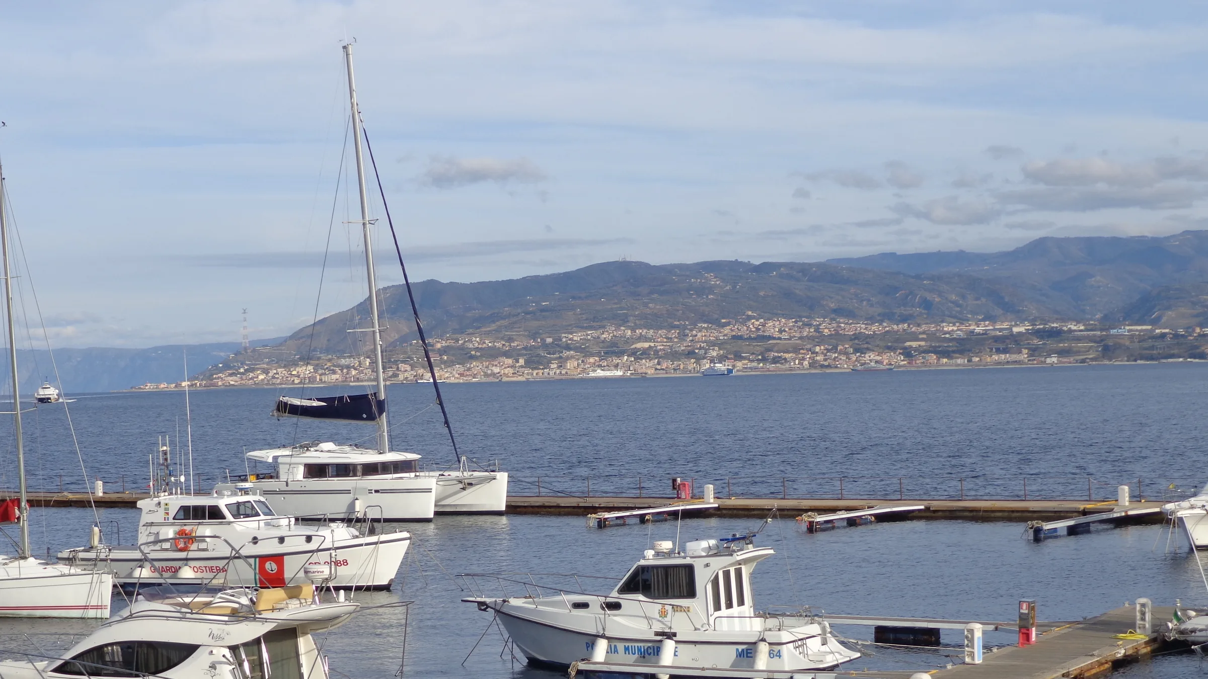Pleasure boats moored in a small marina on the Strait of Messina, with the Calabrian coast across the water.