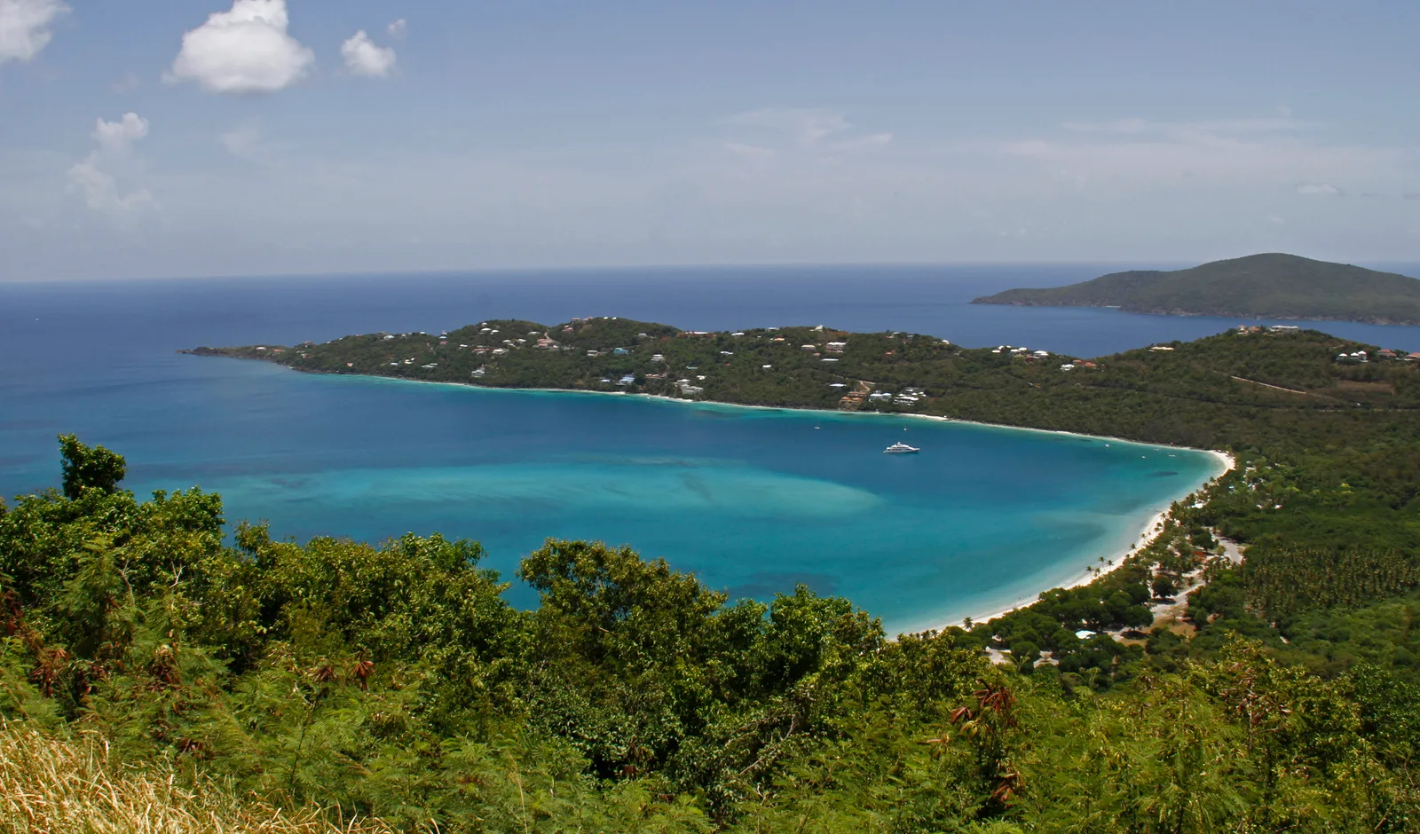 The curved white-sand shoreline of Magens Bay from the hillside lookout with green peninsulas and blue sea.