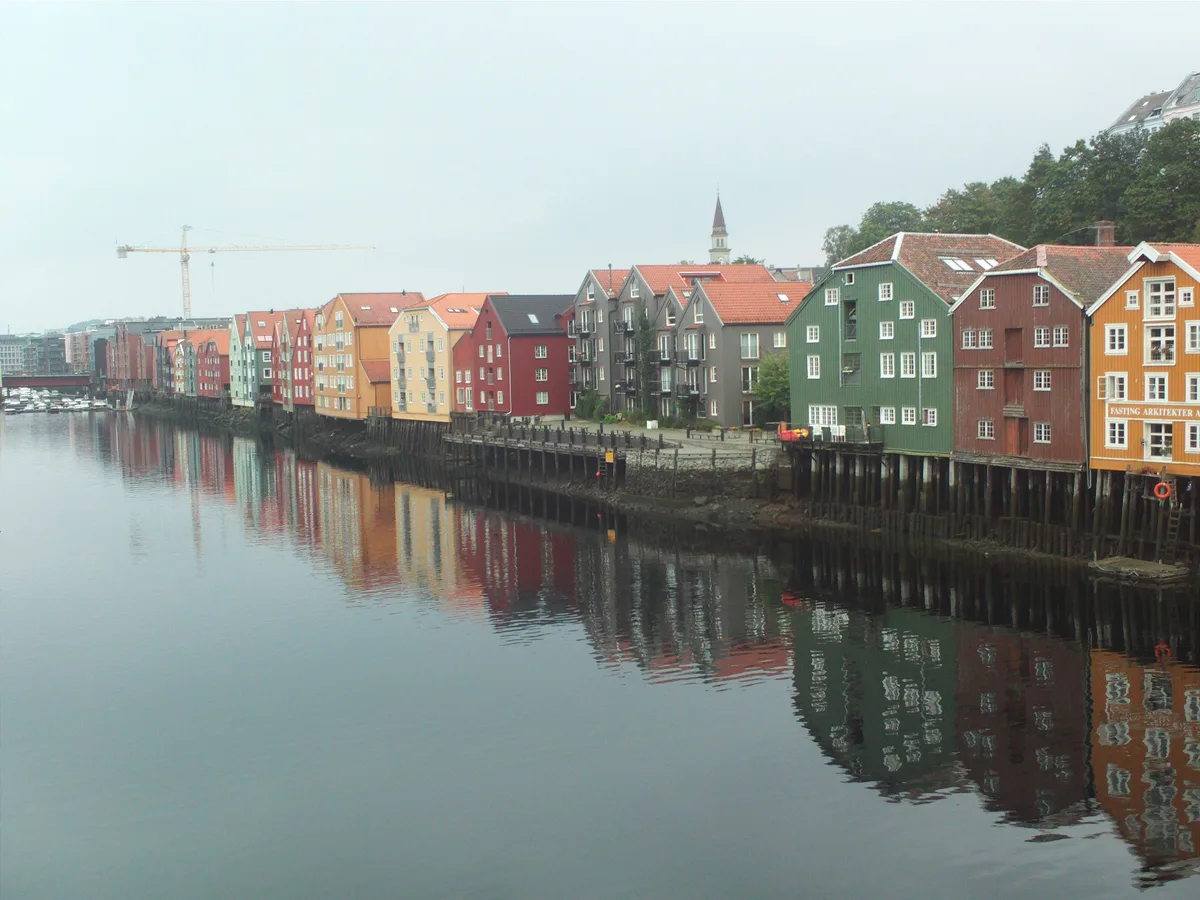 A long row of colourful old storehouses reflected in the calm Nidelva river in Trondheim.
