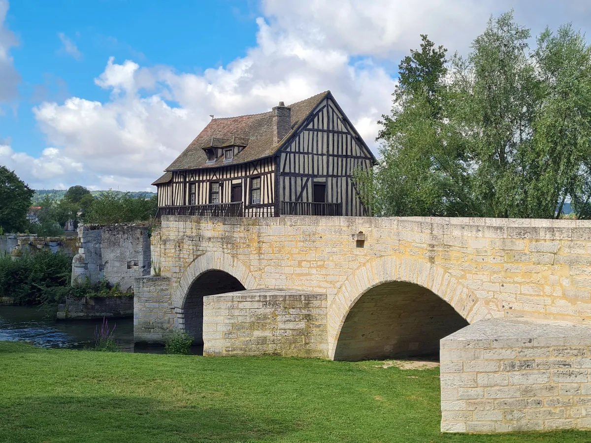 The stone arches of the Vieux Pont at Vernon with the timbered Vieux Moulin built on top and a grass bank.