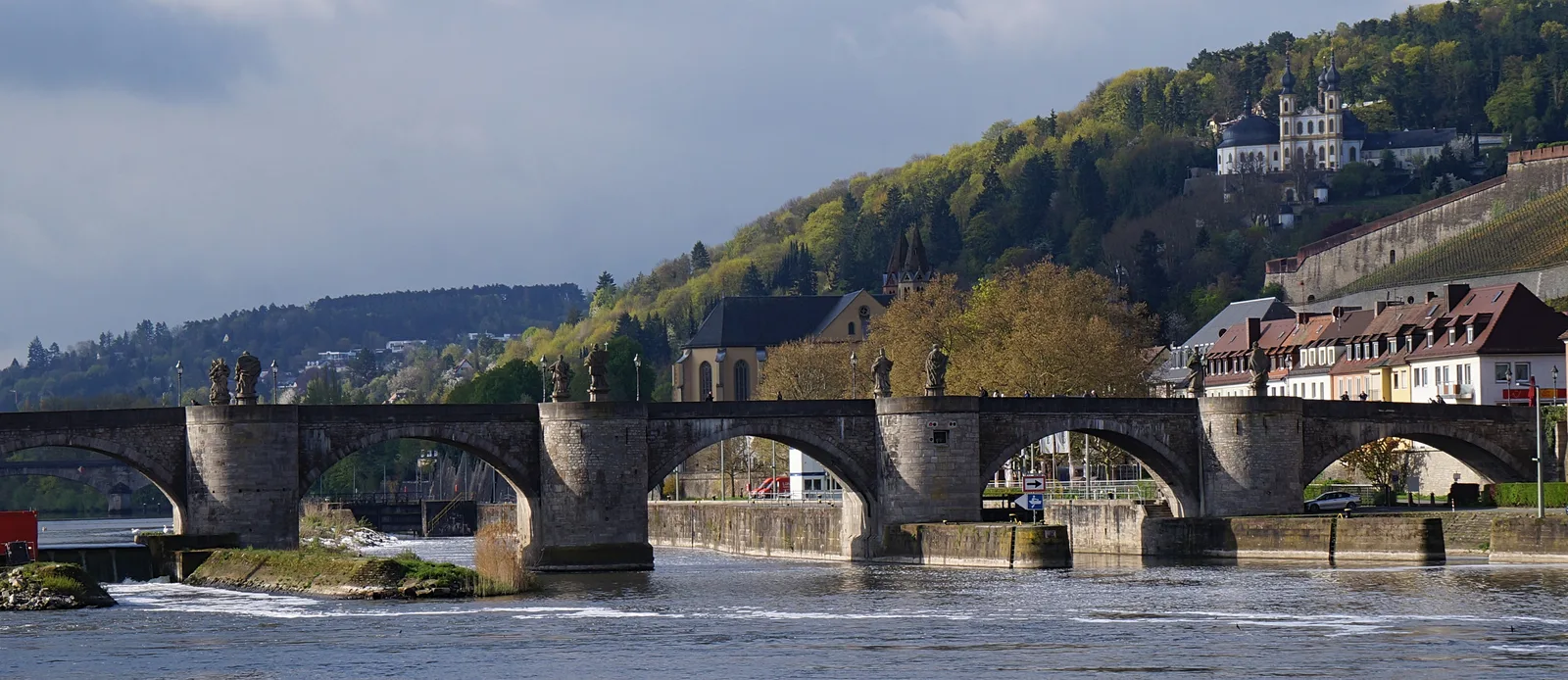 The Old Main Bridge with its stone arches across the Main river in Würzburg and a fortress on the hill behind.
