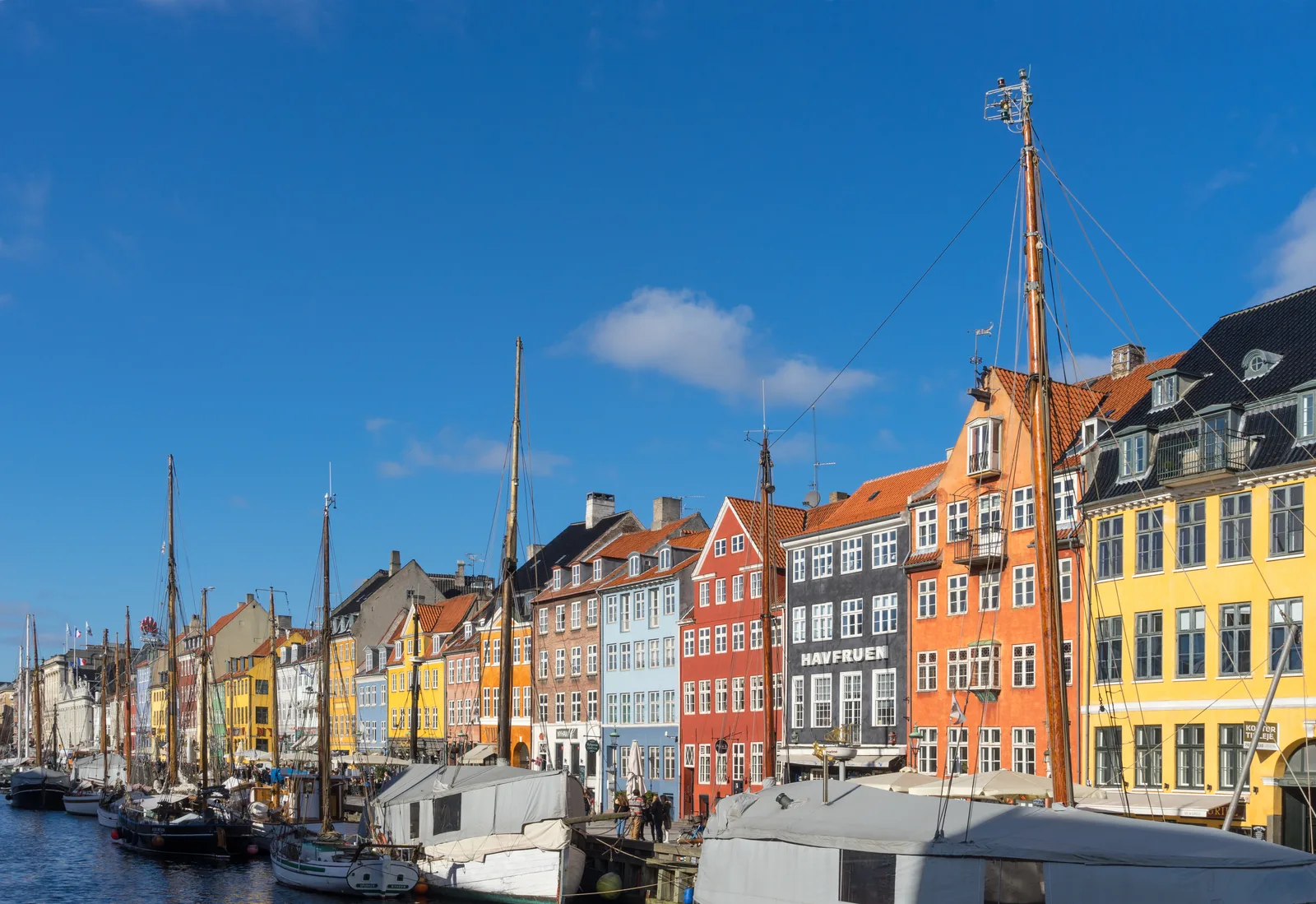 A close view of Nyhavn's yellow, red and green facades with boat masts against a blue sky.