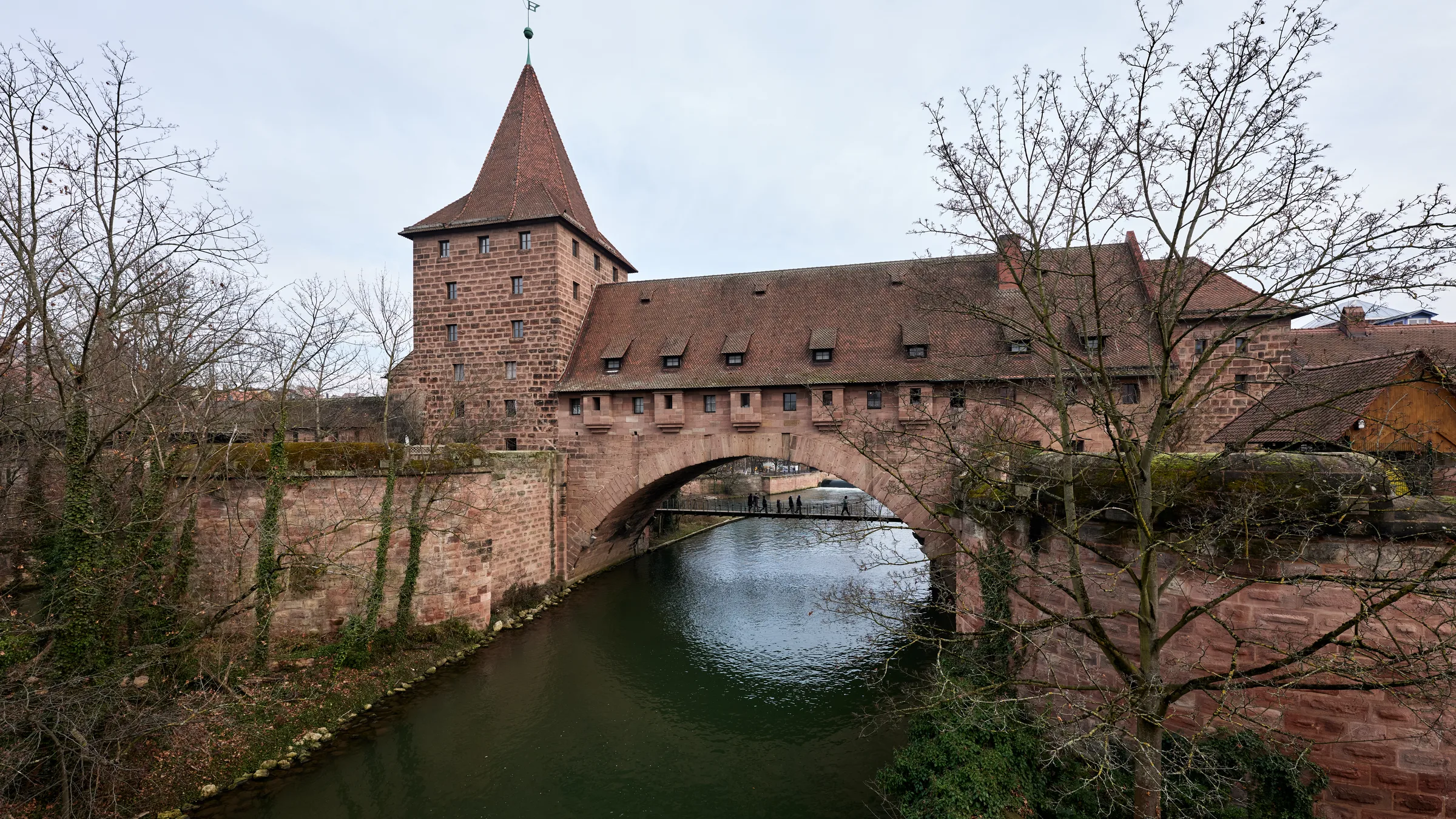 The Hallertor gate tower and the stone arch over the Pegnitz river in Nuremberg, with bare winter trees on the banks.