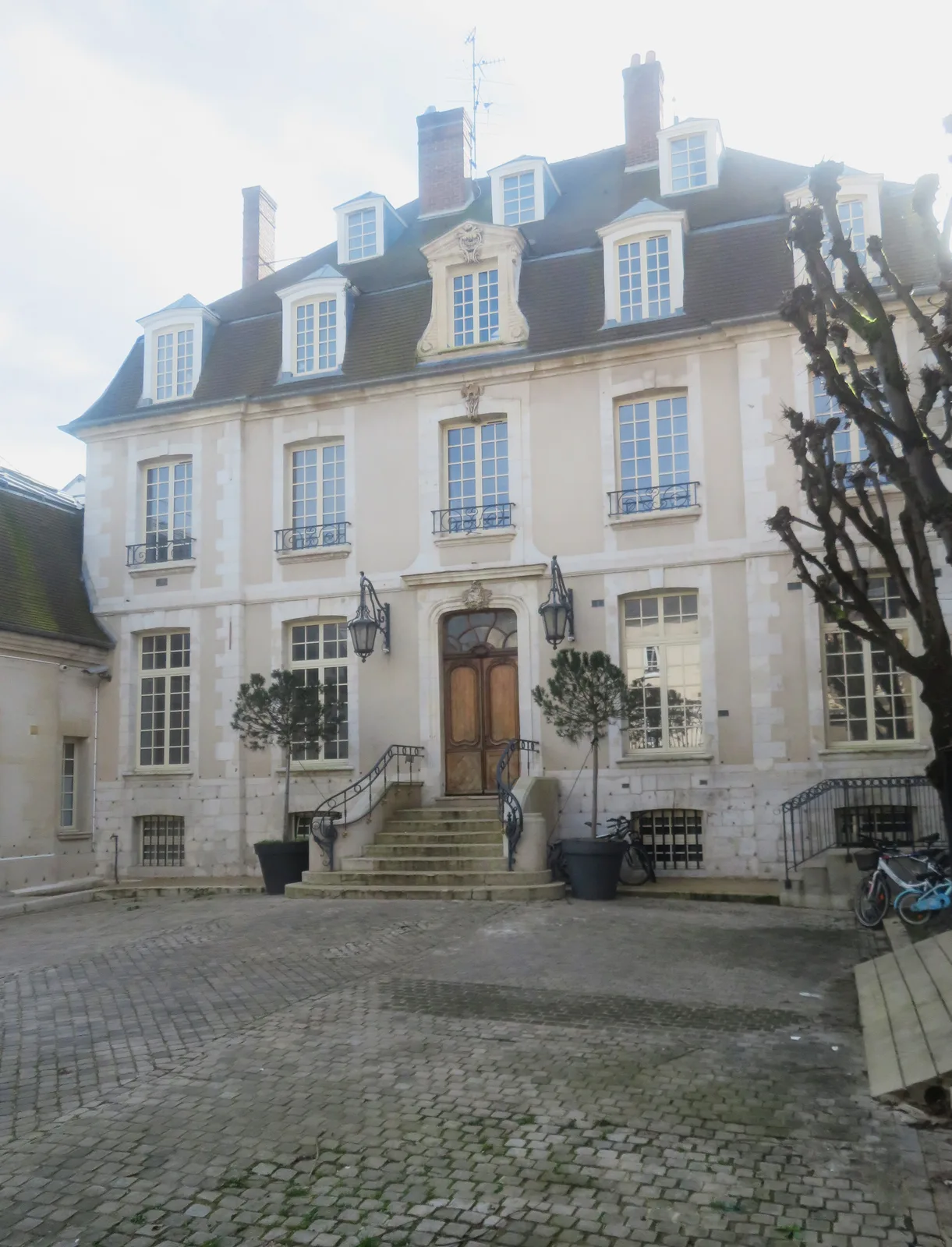 A cream-coloured town house with a mansard roof, steps and a cobbled forecourt in Vernon.
