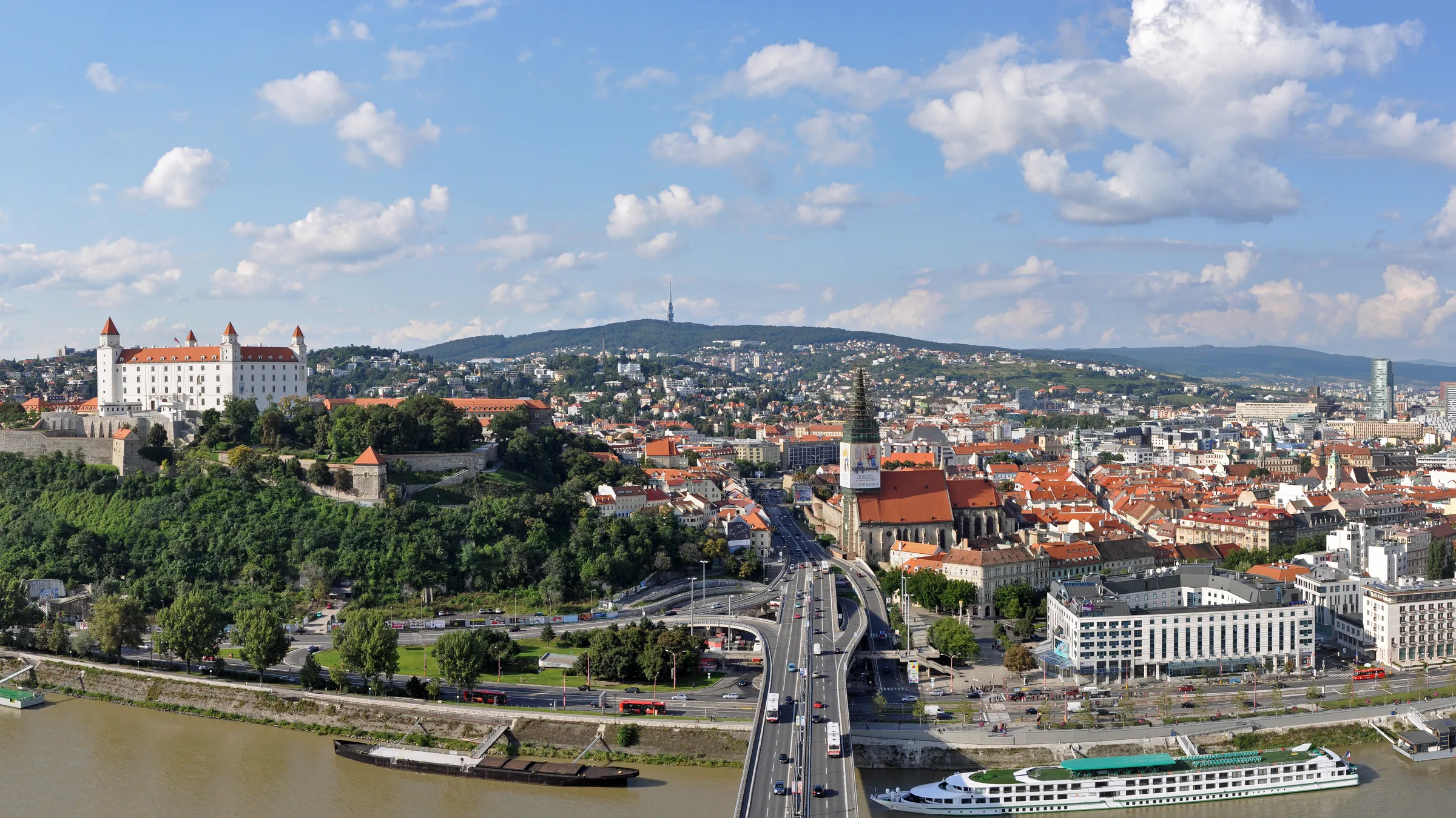 Bratislava Castle on its hill above the old town and the Danube, seen from across the river with a river ship at the quay.