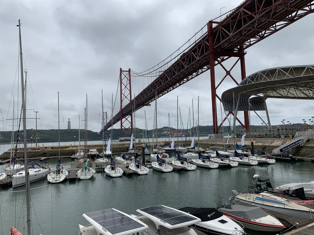 Masts of a marina under the red steel 25 de Abril Bridge in Lisbon.