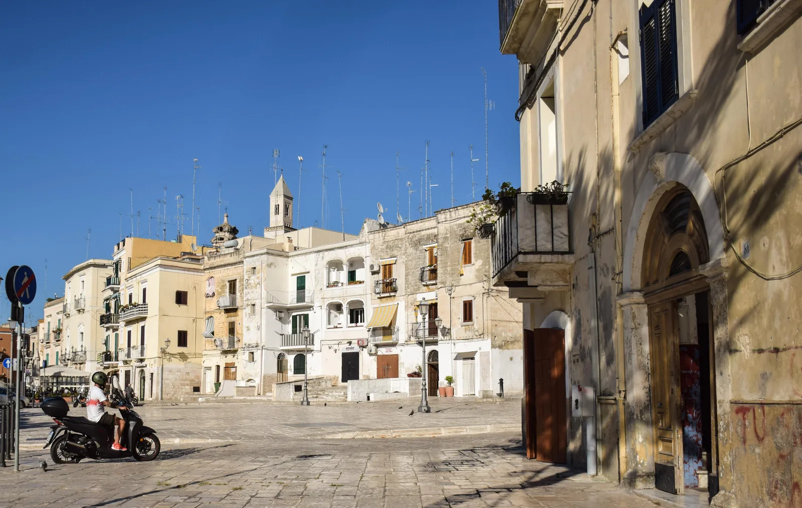 A sunlit square in Bari Vecchia, the old town, with pale stone houses and a bell tower beyond.
